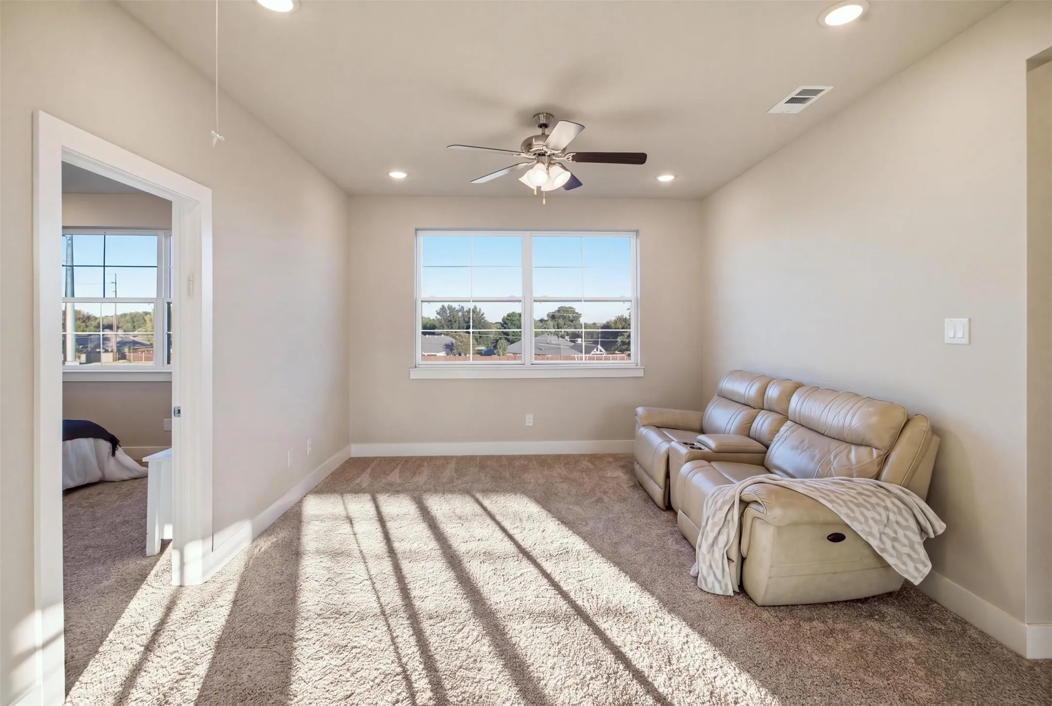 Neutral-toned carpeted interior featuring recessed lighting, a ceiling fan with integrated light fixture, and windows with white muntins