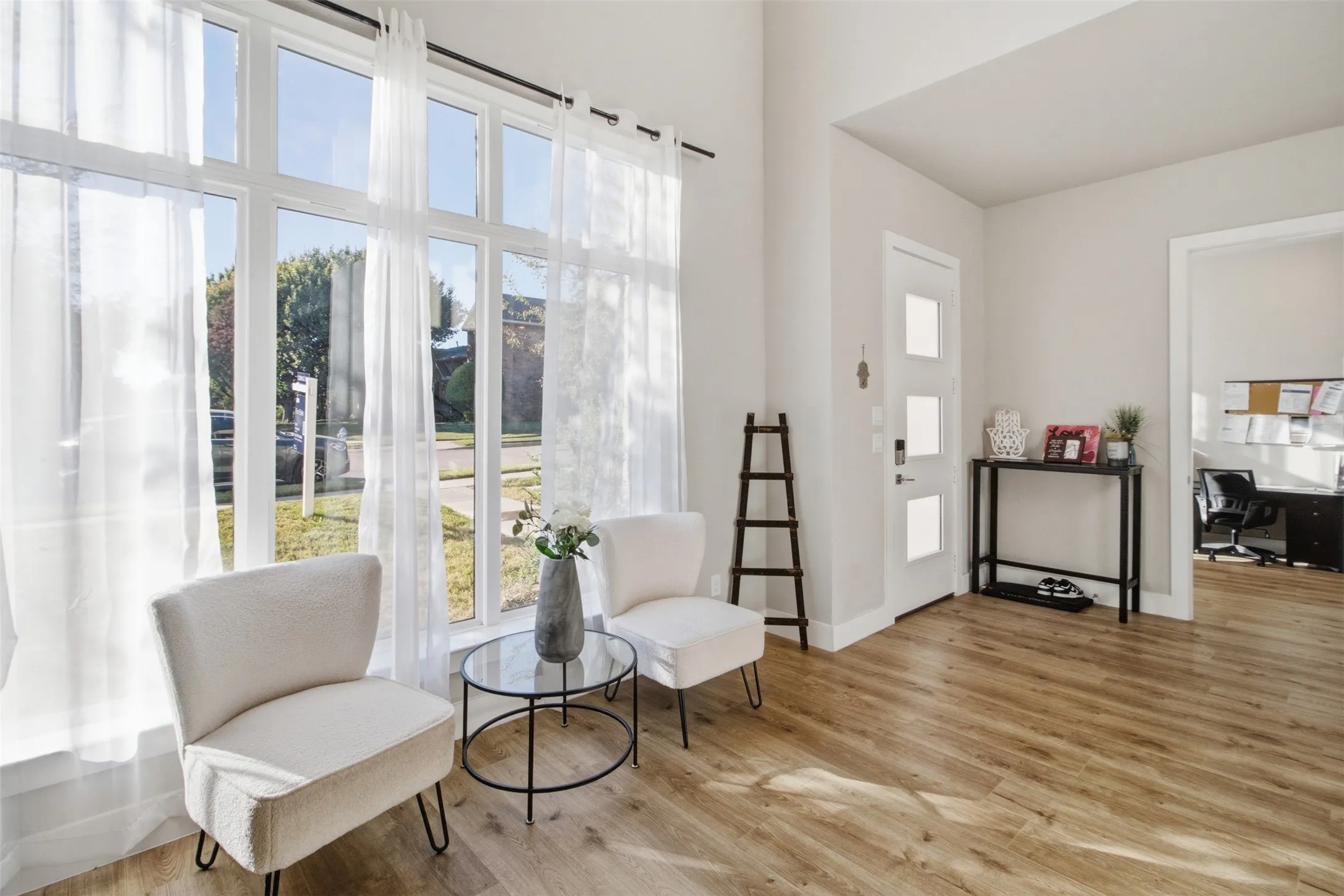 Vaulted ceiling, expansive floor-to-ceiling windows, white entry door with frosted glass panels, and wood-finish flooring