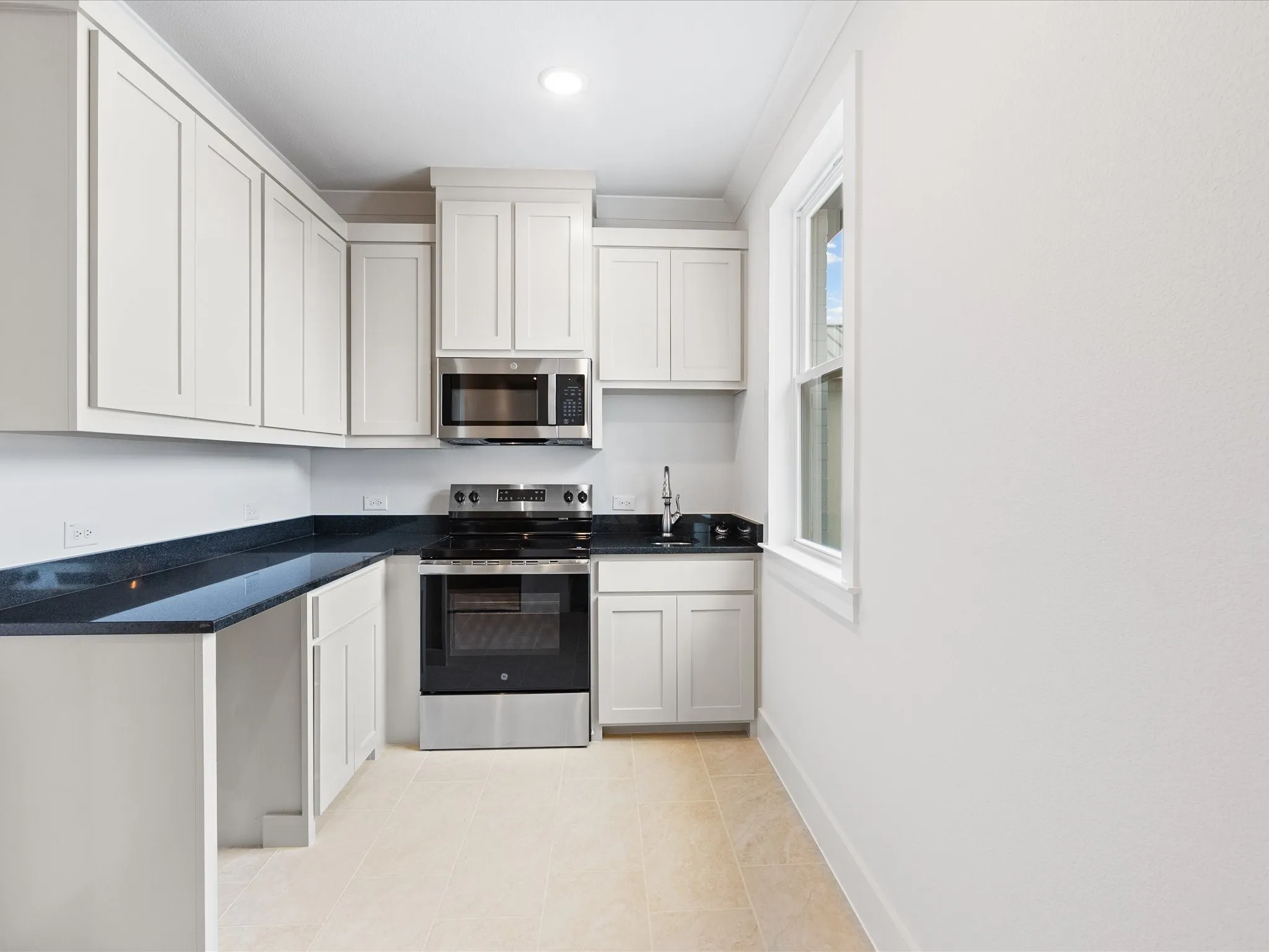 Kitchen featuring white shaker-style cabinetry, dark stone countertops, stainless steel appliances, and tile flooring
