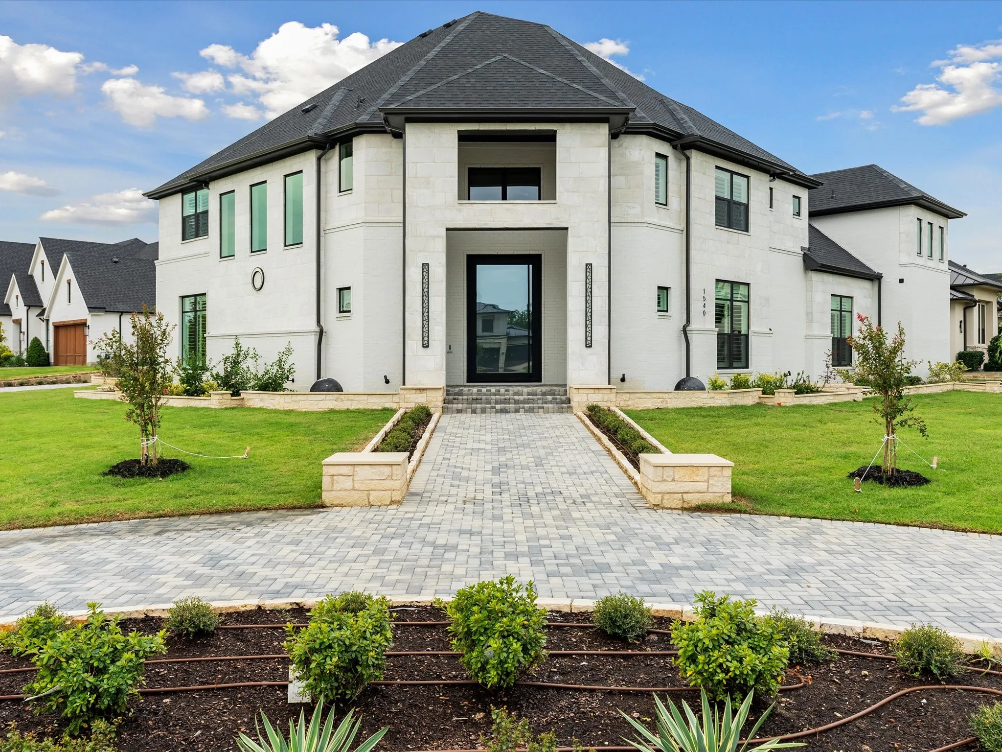 Custom masonry exterior featuring stone facade, multi-faceted roofline, pavers walkway, covered entryway, and multi-pane dark-framed windows
