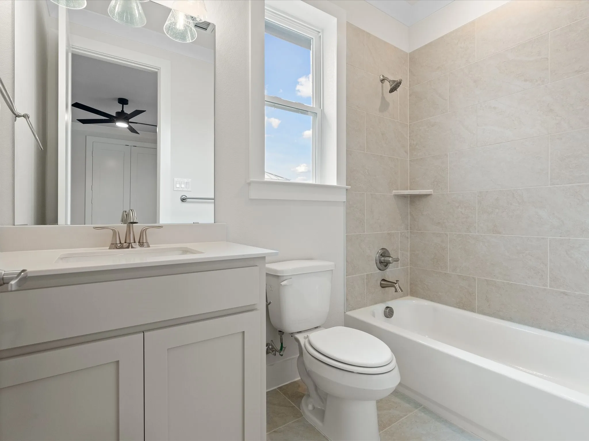 Bathroom featuring a vanity with a white countertop and undermount sink, tiled bathtub surround with a built-in shelf, brushed nickel hardware, and neutral tile flooring