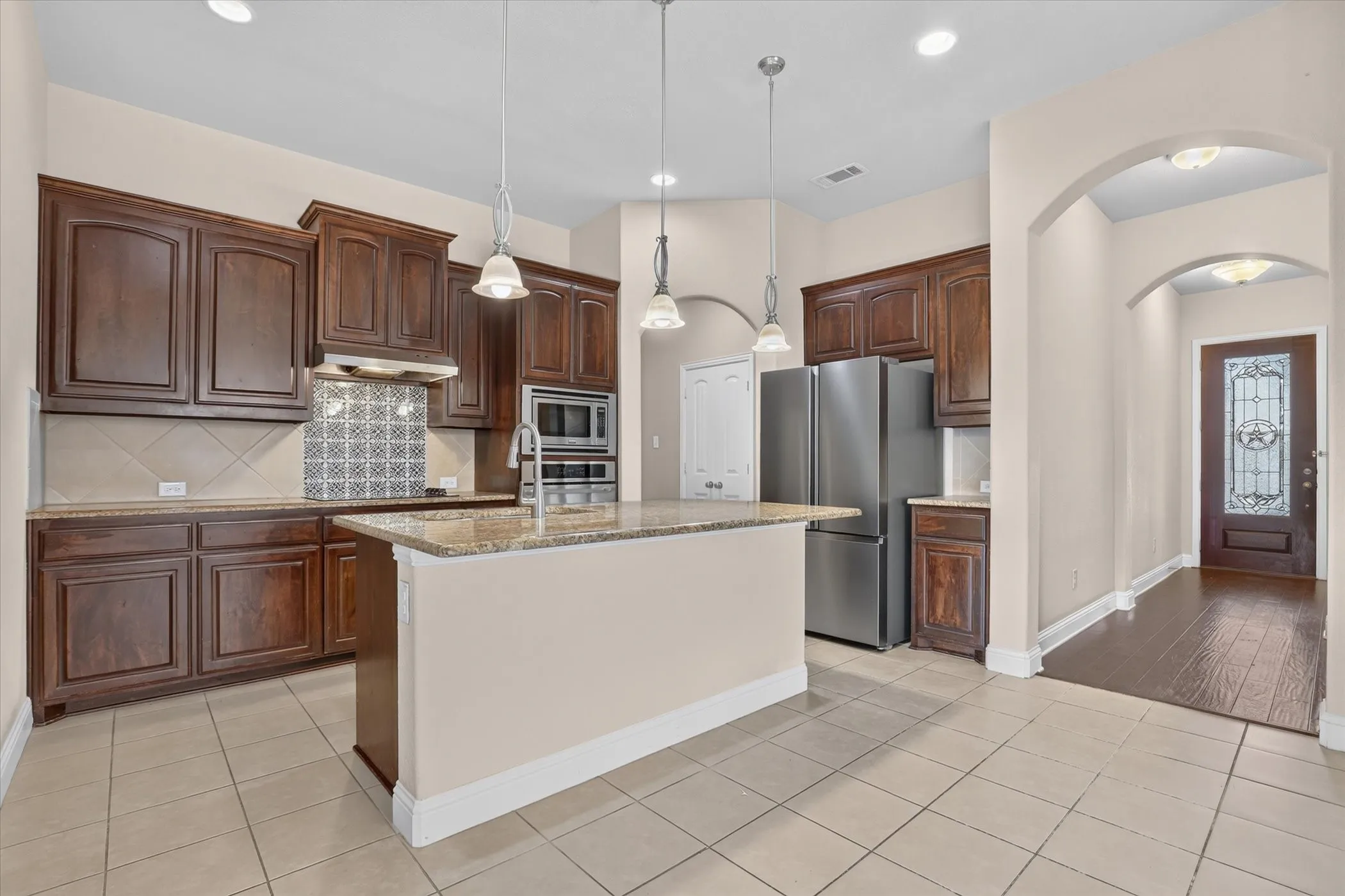Kitchen featuring wood cabinetry, stone countertops, decorative tile backsplash, stainless steel appliances, and pendant lighting
