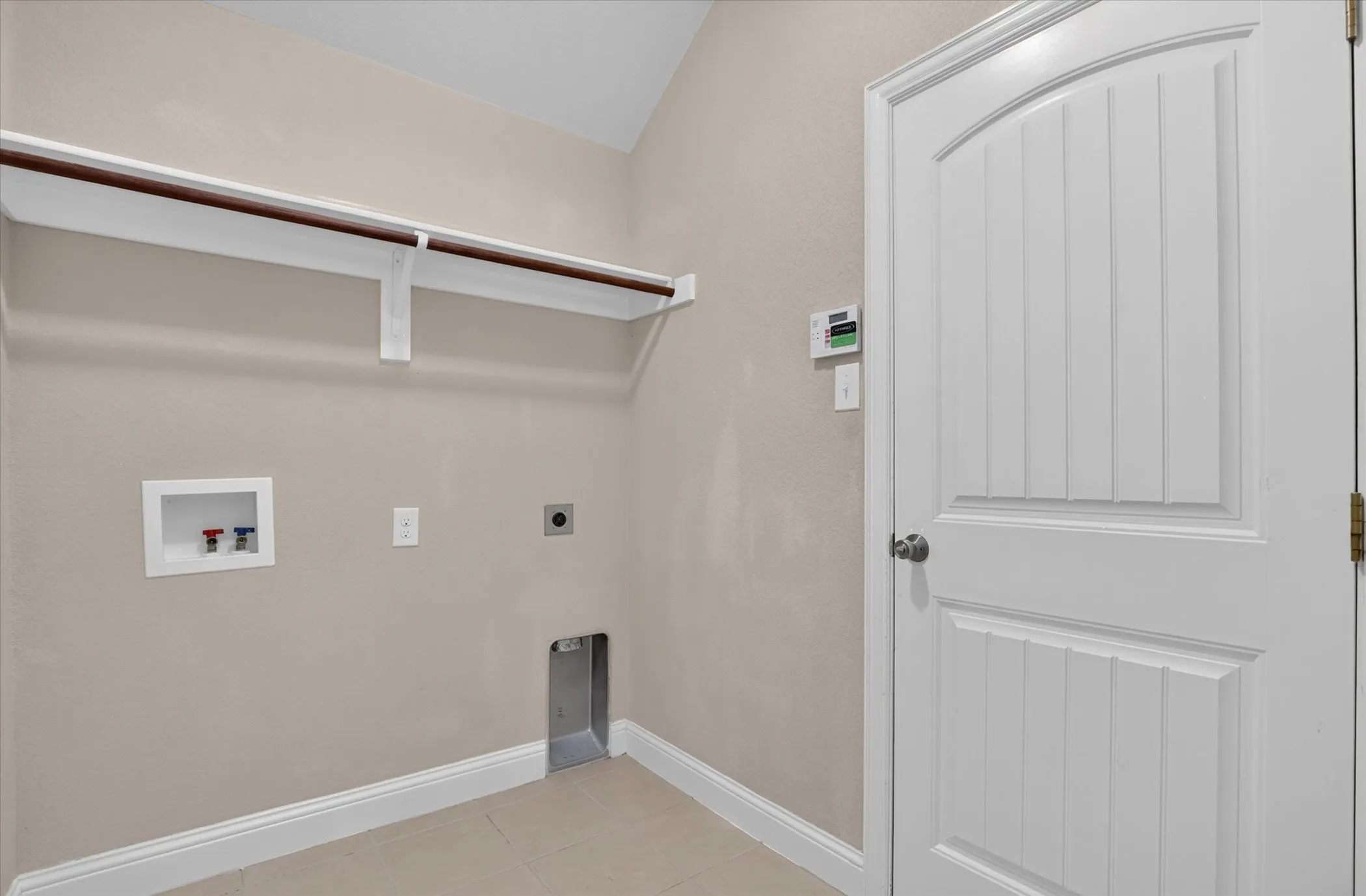 Utility space featuring neutral wall tones, a built-in shelf with hanging rod, tile flooring, and a six-panel door