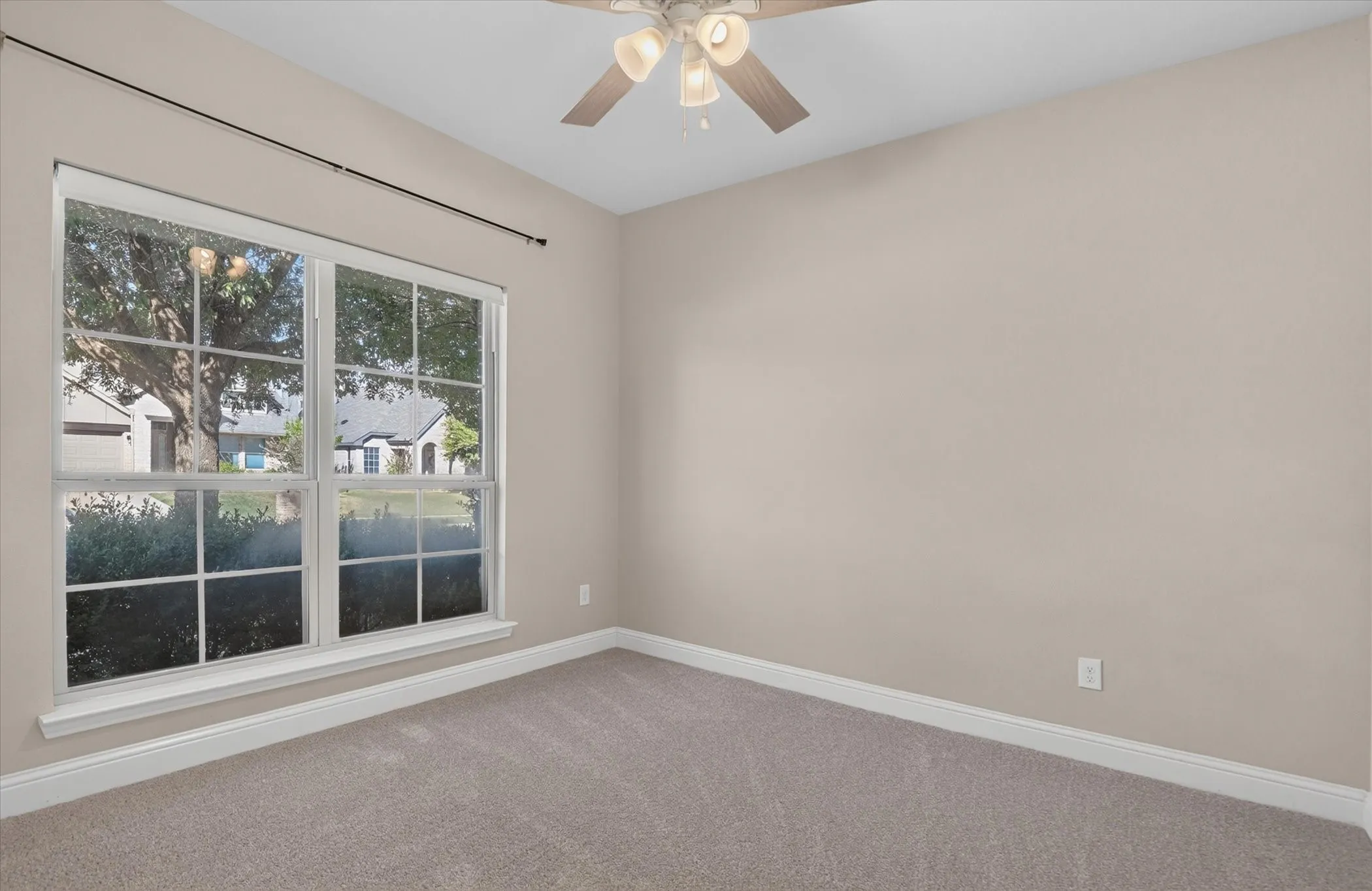 Neutral interior room featuring wall-to-wall carpeting, a multi-pane window with grid detailing, and a ceiling-mounted fan with integrated lighting
