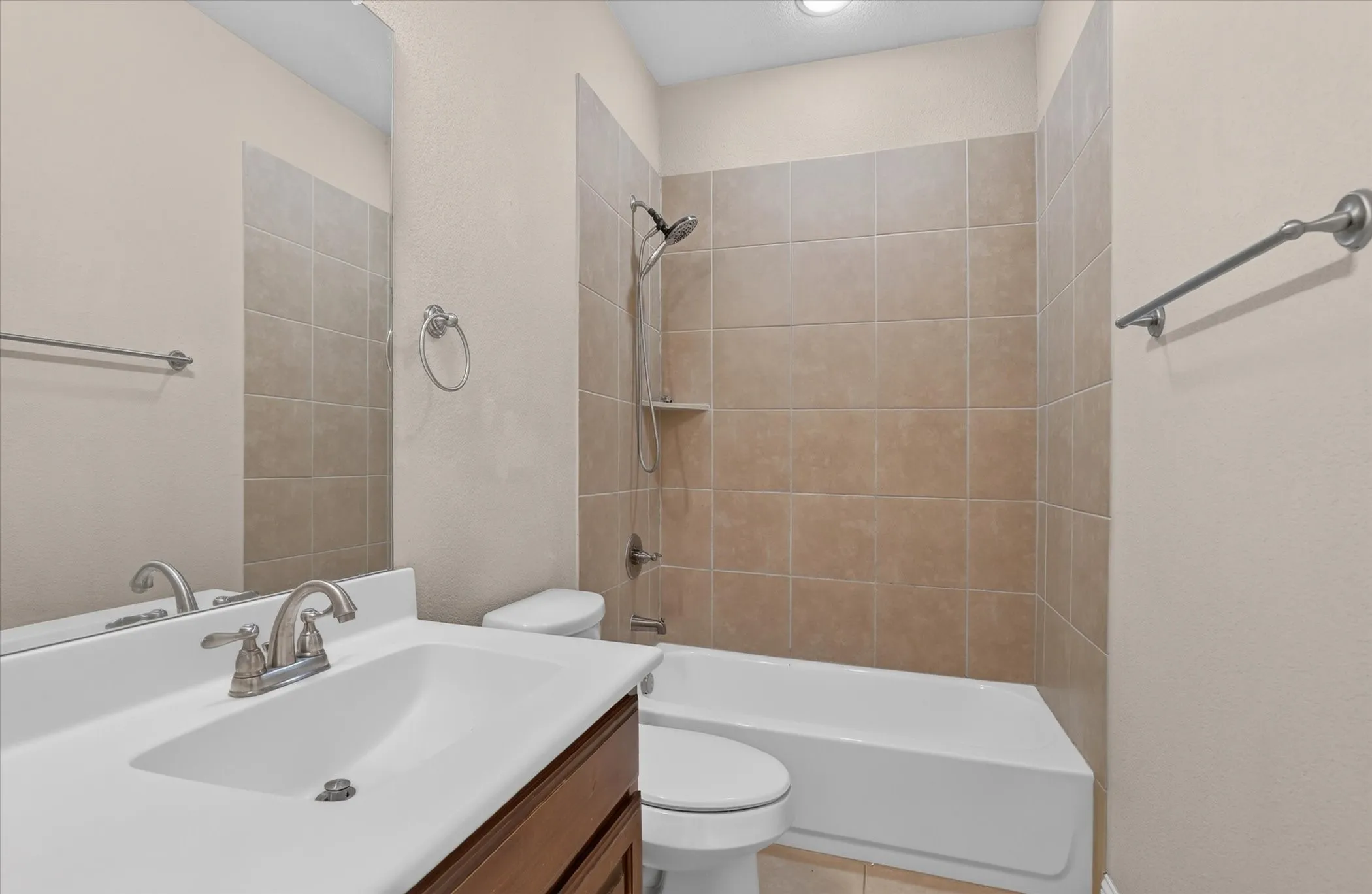 Bathroom featuring a single-sink vanity with an integrated countertop, wood-finish cabinetry, tile-surround tub-shower combination, and polished chrome hardware