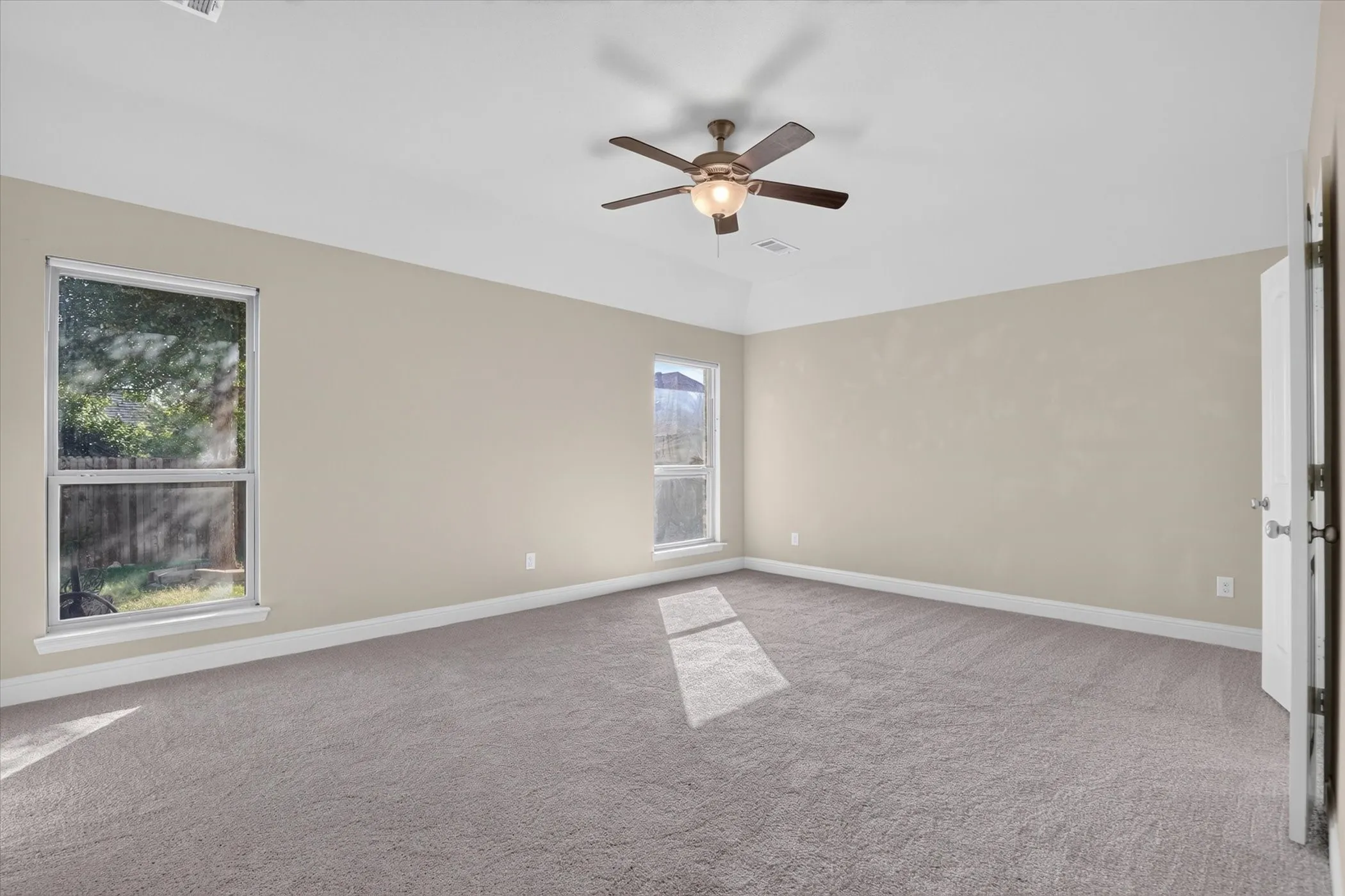 Room featuring a tray ceiling, wall-to-wall carpeting, dual windows, and a central ceiling fan with an integrated light fixture