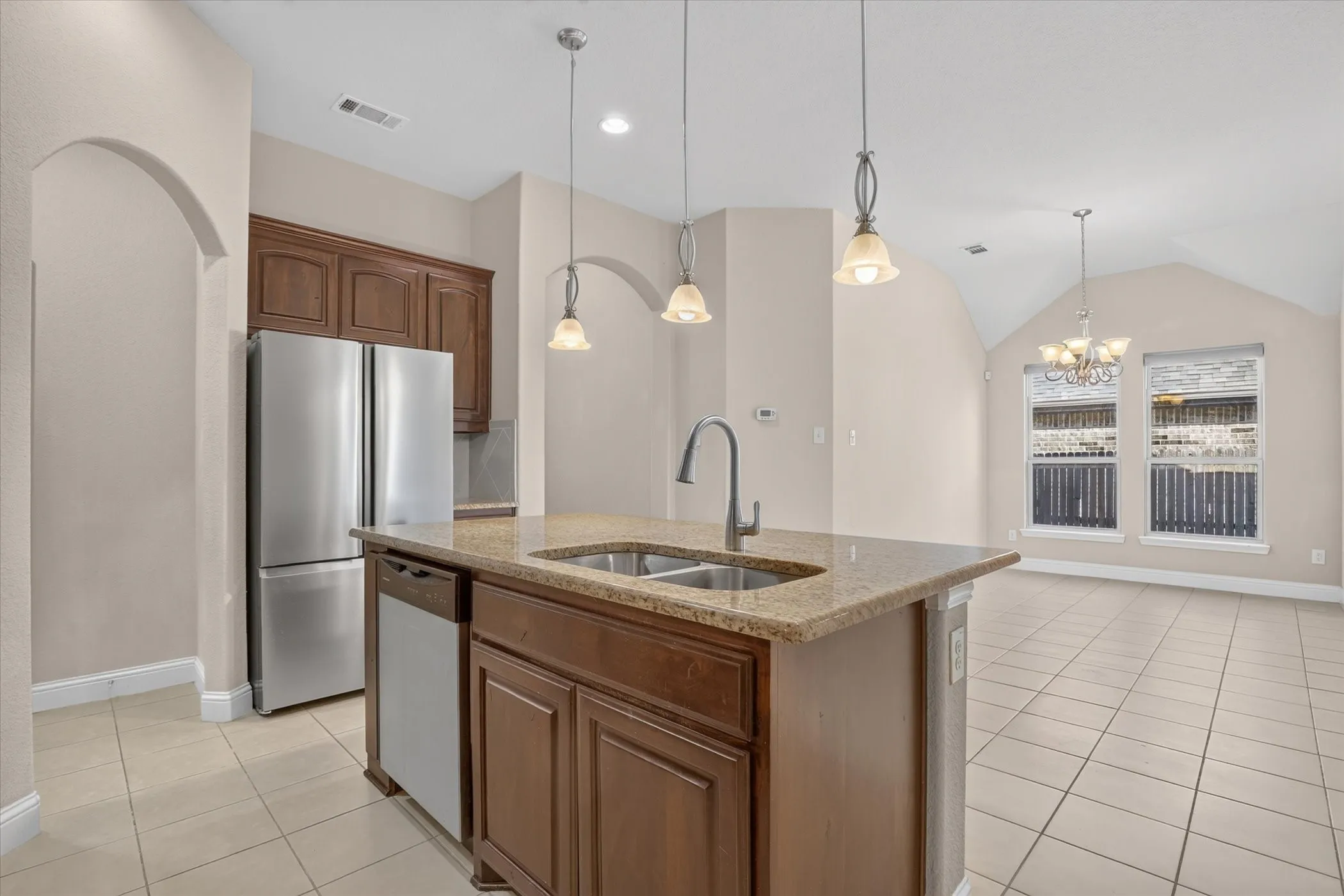 Kitchen featuring stone countertops, a center island with an undermount double-basin sink, stainless steel appliances, stained wood cabinetry, and pendant lighting