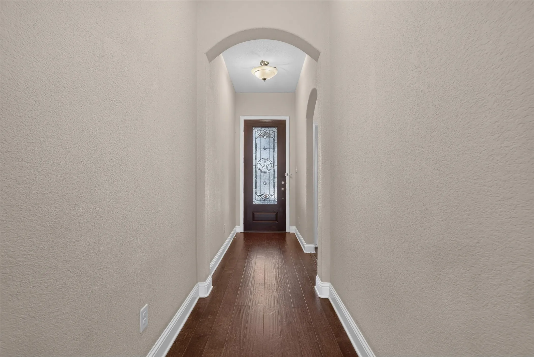 Entryway featuring dark-stained wood-finish flooring, a decorative door with glass inlay, an arched ceiling detail, and a flush-mount light fixture