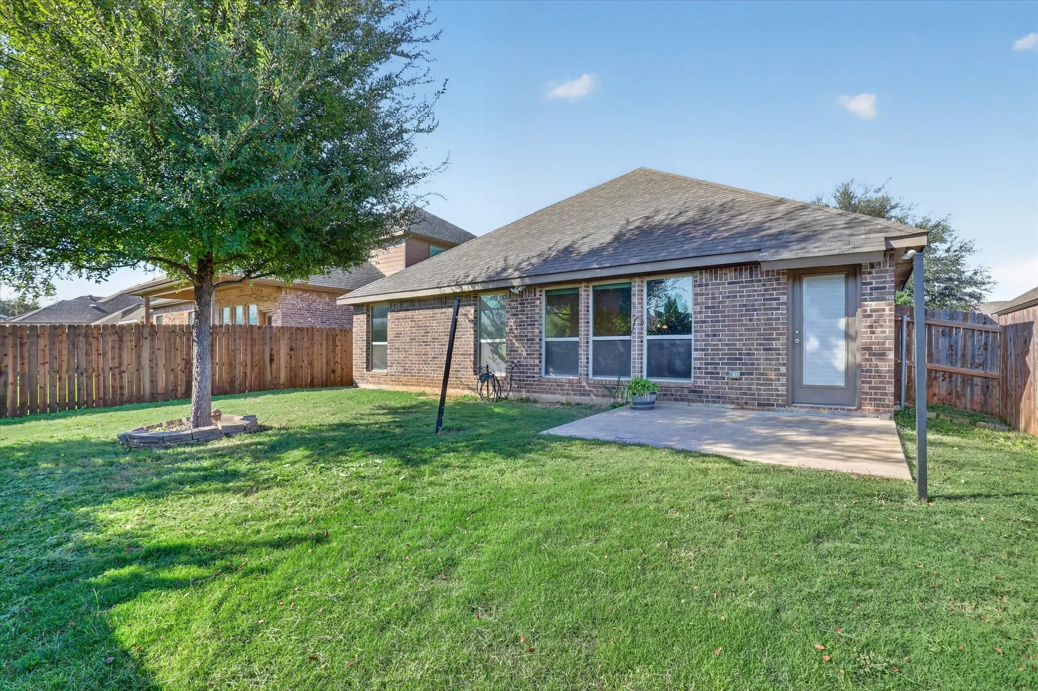 Brick exterior featuring a concrete patio, wood privacy fencing, and a mature tree