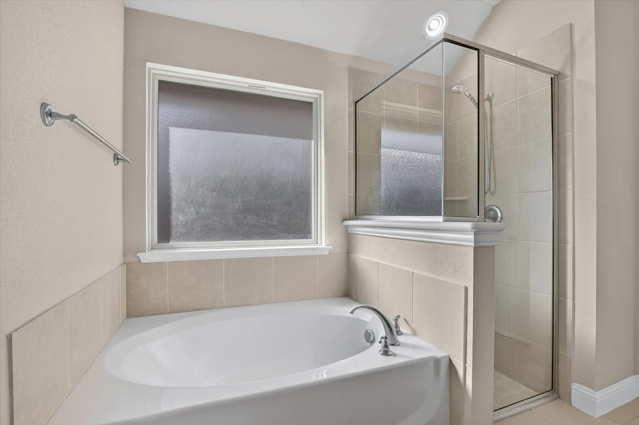 Bathroom featuring a deep soaking tub with a deck-mounted faucet, a separate glass-enclosed shower, neutral tile surround, and a large window