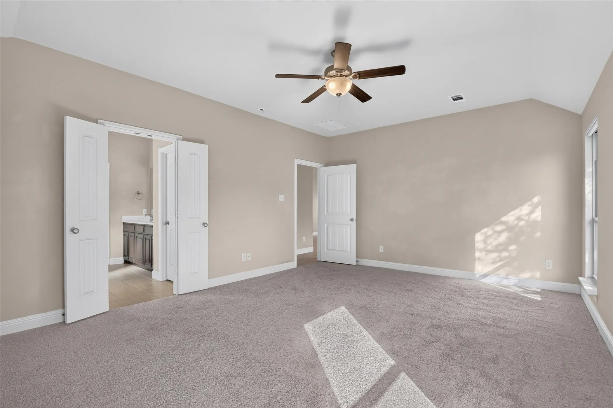 Vaulted ceiling featuring a central multi-blade ceiling fan with integrated light fixture, neutral wall palette, and wall-to-wall carpeting