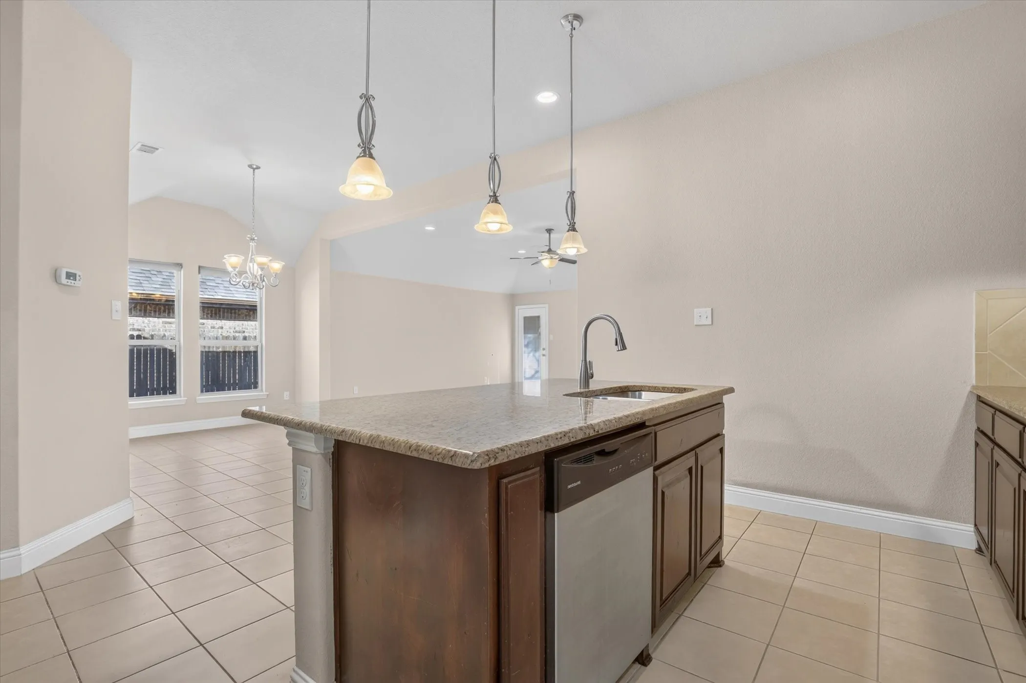 Kitchen island featuring a neutral-toned stone countertop, integrated stainless steel dishwasher, undermount sink, and three pendant lights, complemented by tile flooring throughout