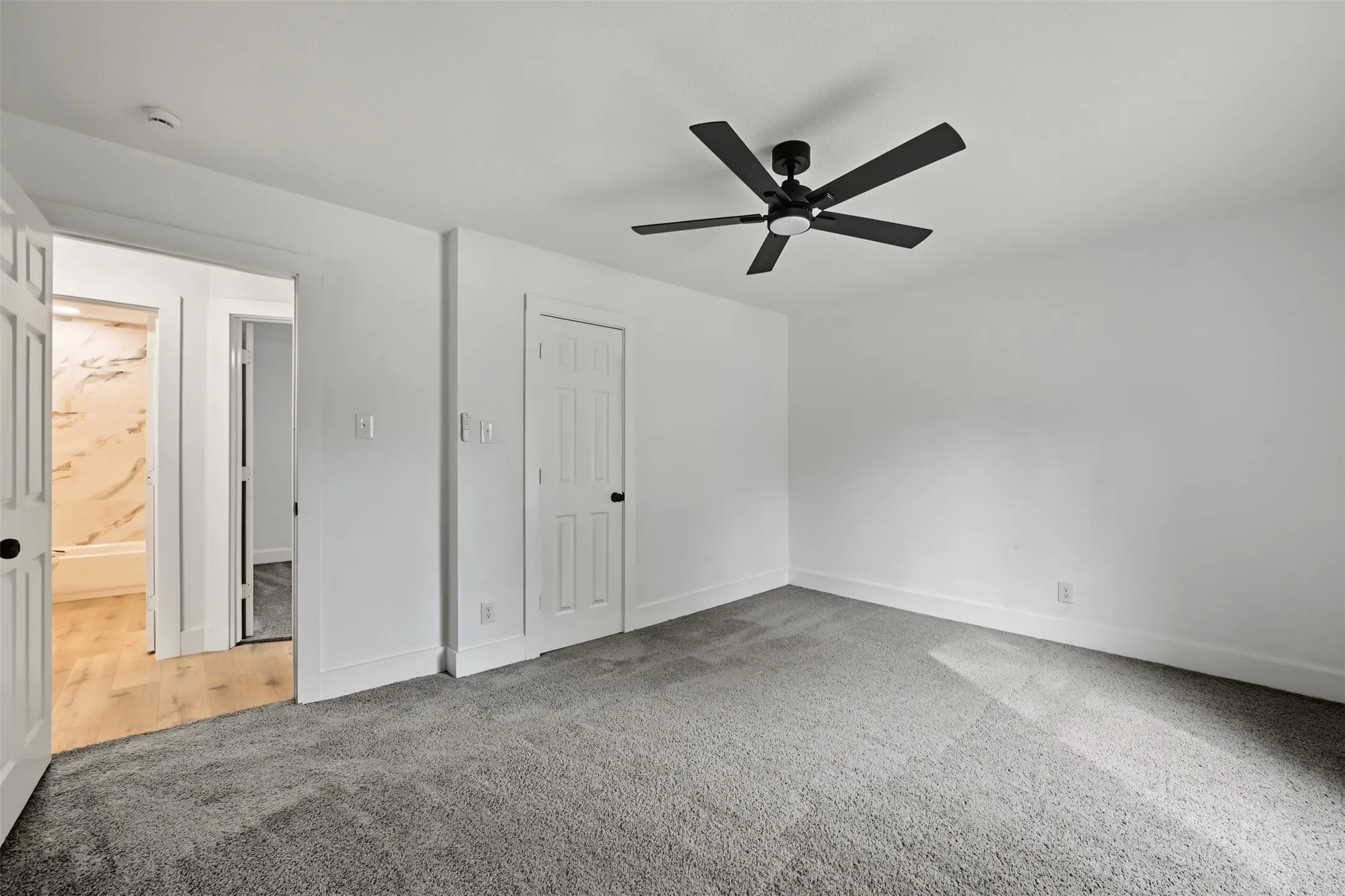 Interior room featuring neutral wall-to-wall carpeting, a matte black five-blade ceiling fan, and a six-panel interior door