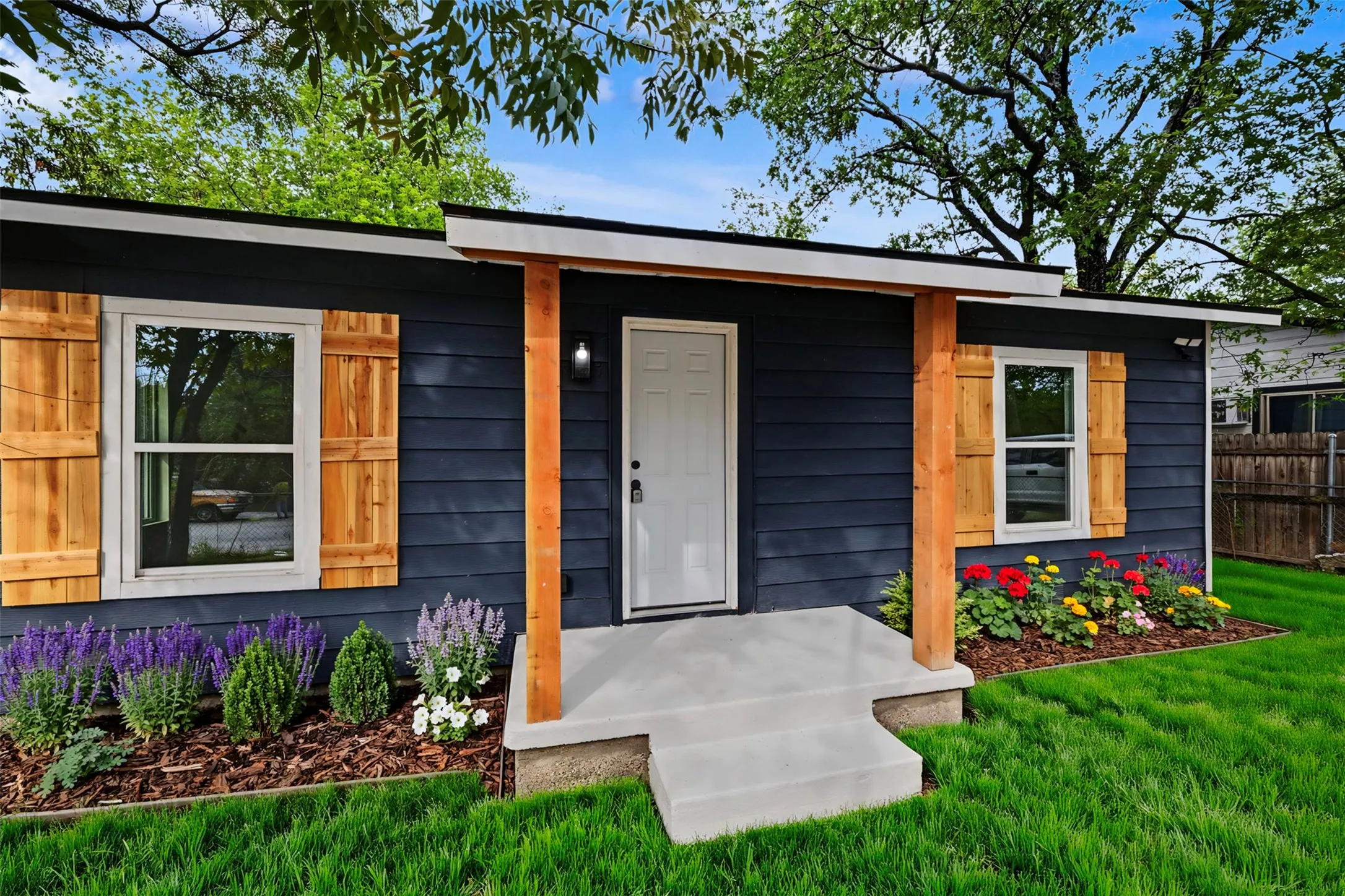 Dark-tone horizontal siding exterior featuring natural wood-finish shutters, a covered porch with exposed timber supports, and a concrete entry pad