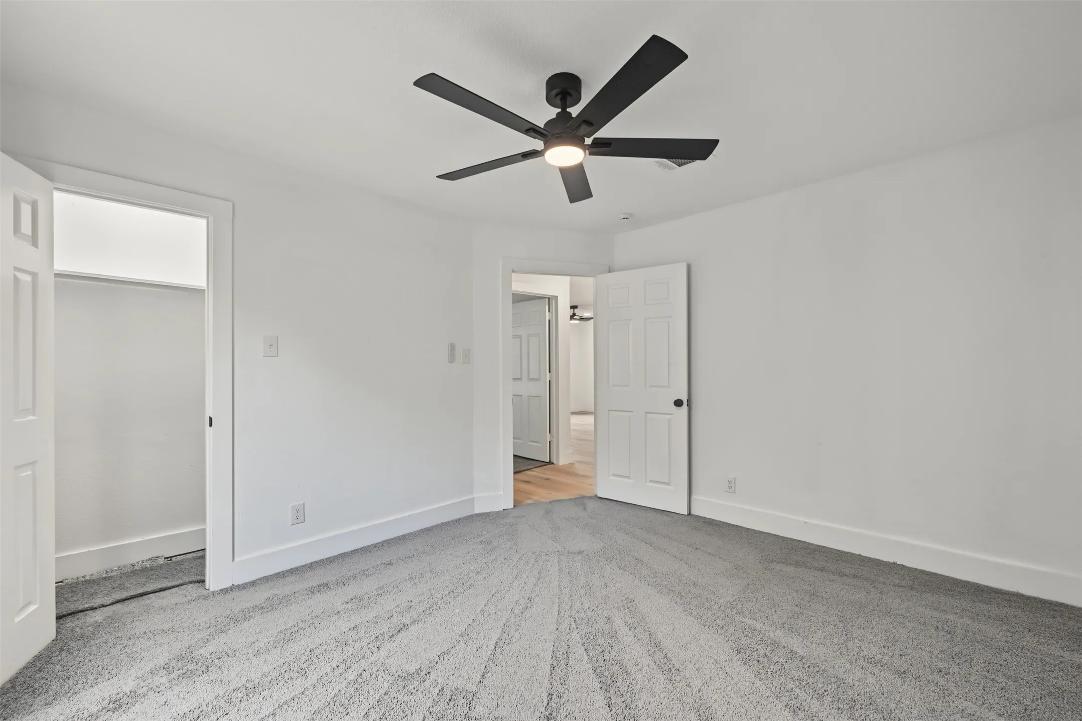 Neutral-toned wall-to-wall carpeting, matte black six-blade ceiling fan with integrated light fixture, and solid-core six-panel interior doors