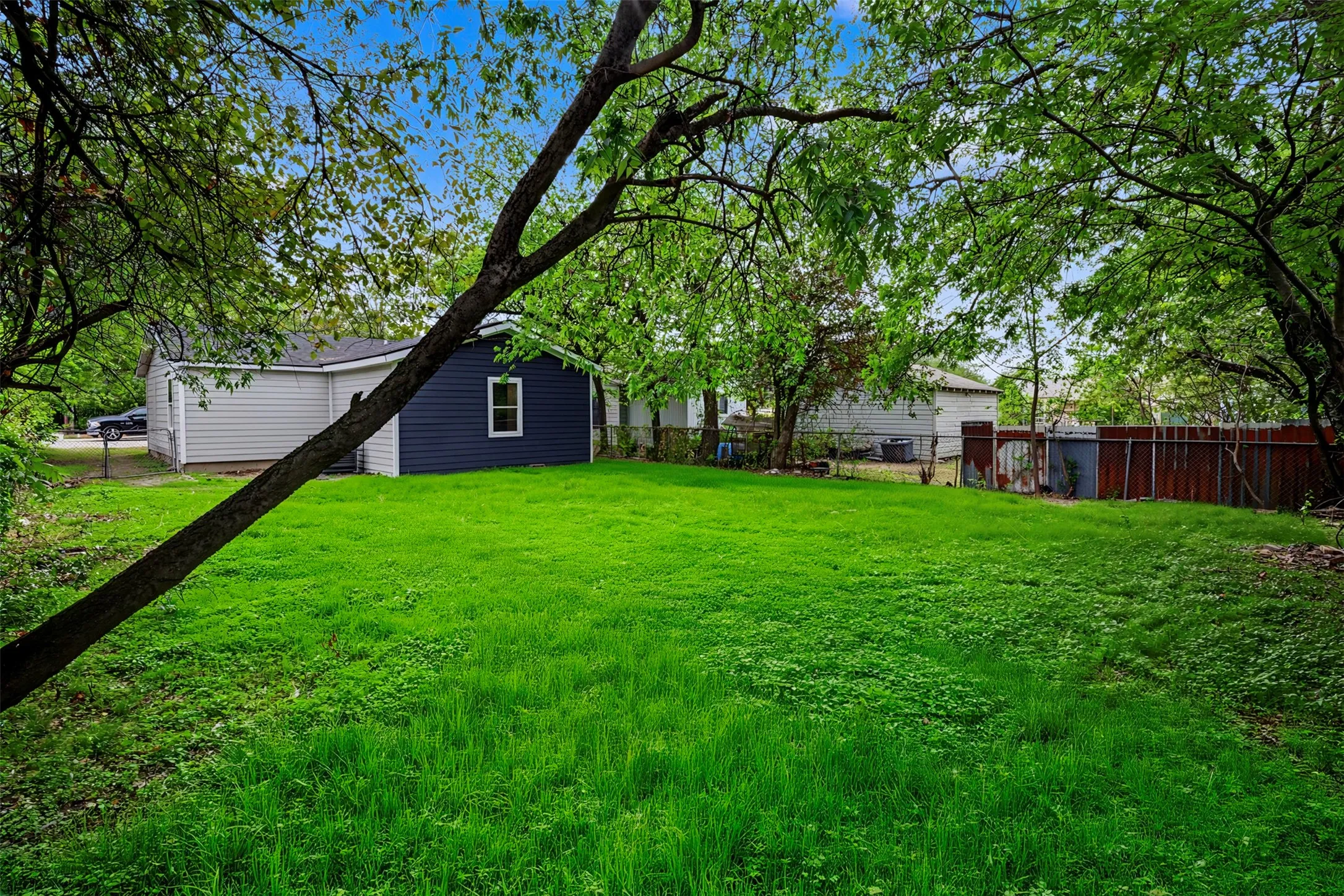 Expansive backyard featuring a level lawn, mature trees, and perimeter wood fencing