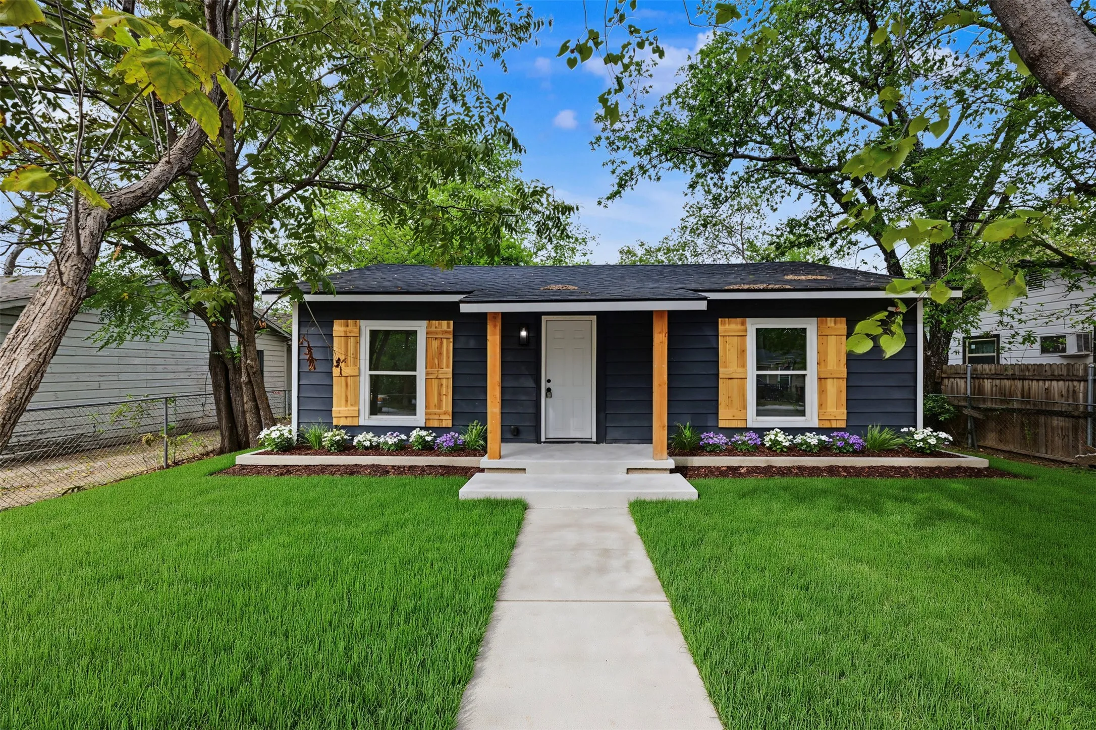 Exterior featuring navy lap siding, natural wood-finish window shutters, a covered porch with wood support posts, and concrete hardscaping