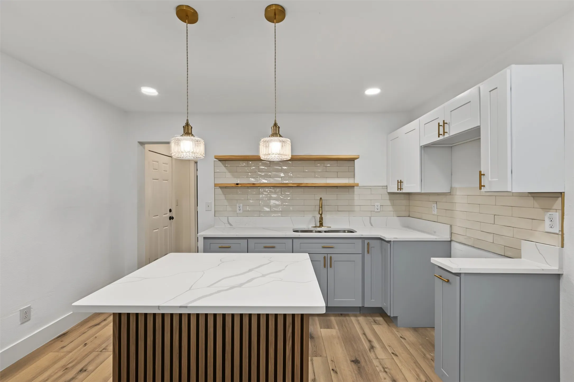 Kitchen featuring a center island with slat wood-finish detailing, stone-composite countertops with veining, subway tile backsplash, shaker-style cabinetry, and dual pendant lighting