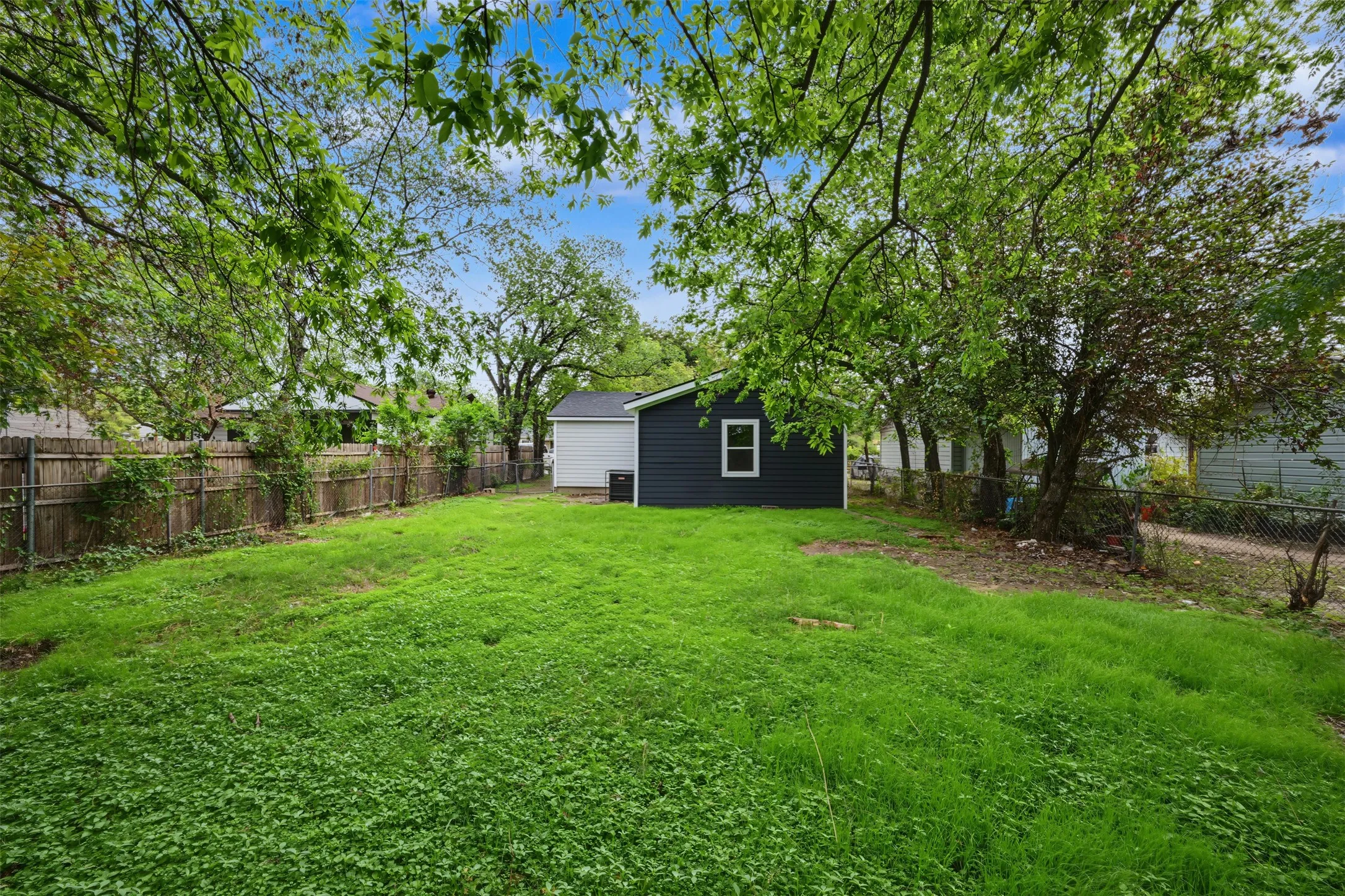 Expansive backyard featuring a large grass lawn, mature trees, and perimeter wood fencing