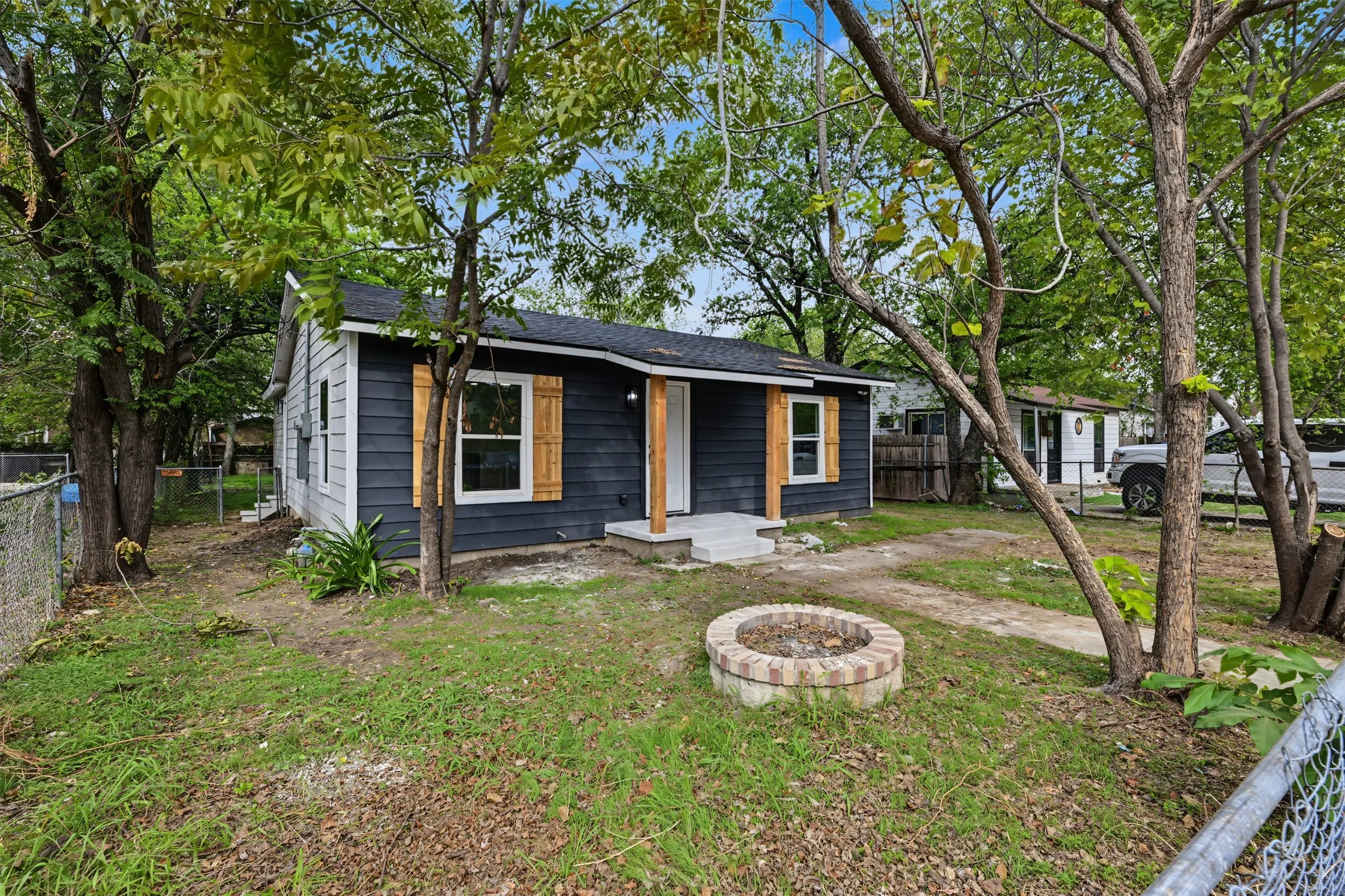 Dark-hued siding, natural wood shutters, covered front porch, and a circular stone fire pit