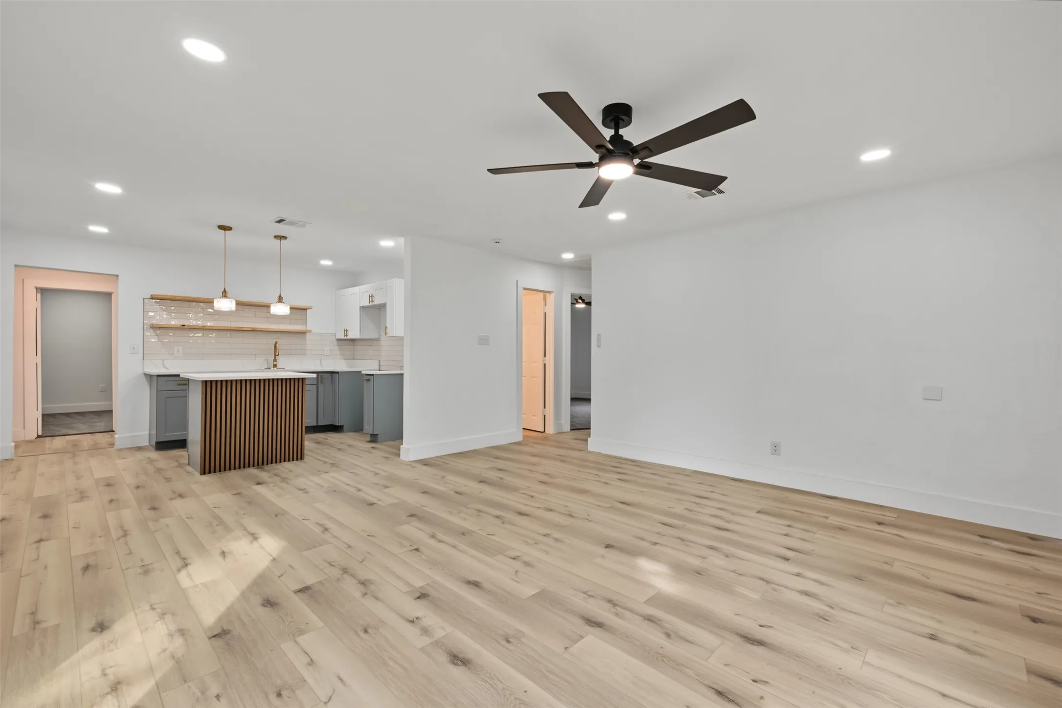 Open-concept interior featuring light-tone wood-finish flooring, recessed lighting, and a modern ceiling fan