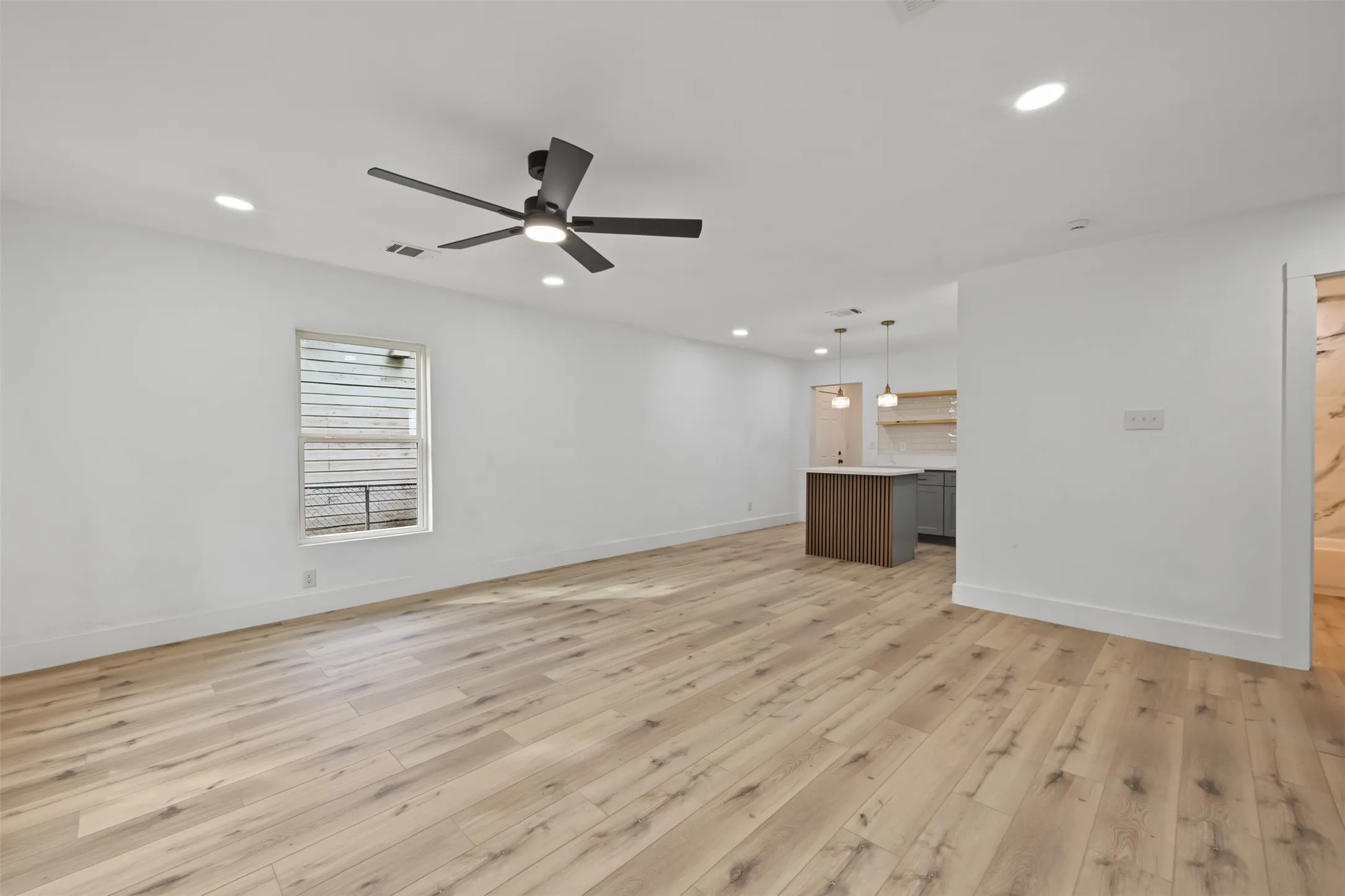 Open-concept interior featuring light-tone wood-finish flooring, recessed lighting, and a modern ceiling fan with integrated lighting