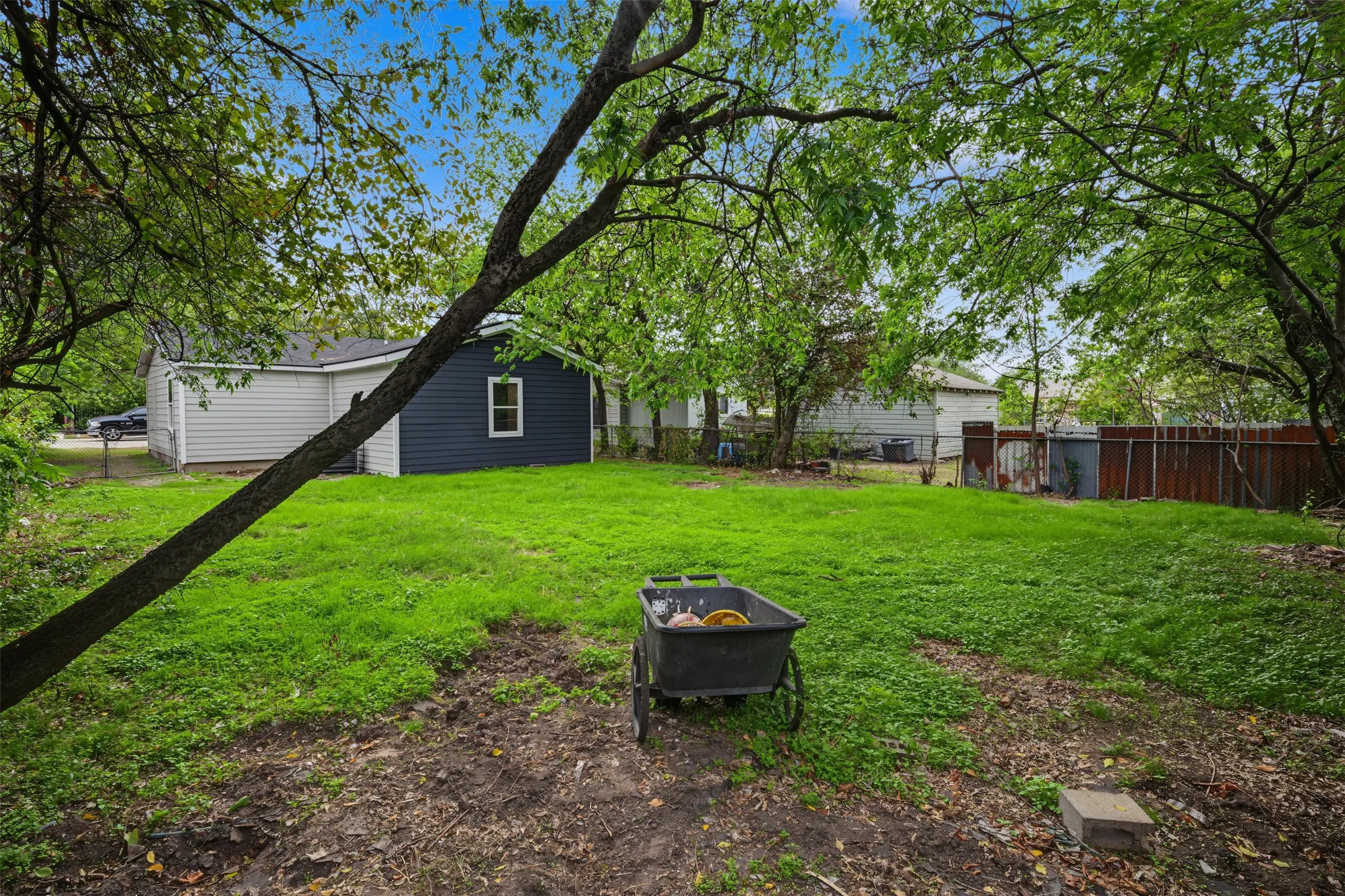 Expansive backyard featuring a grass lawn, mature trees, and perimeter wood fencing