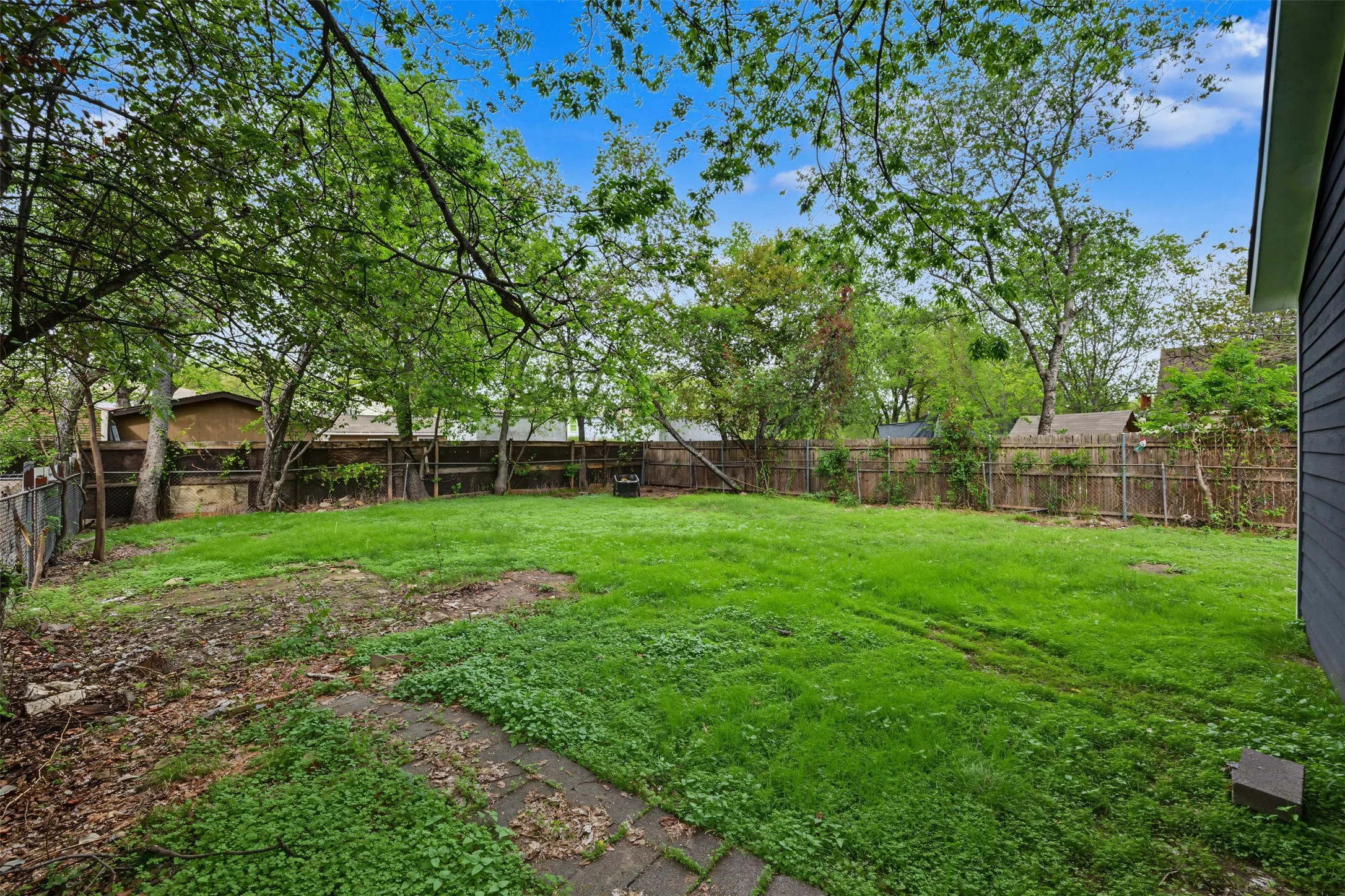 Private backyard featuring an expansive lawn, mature shade trees, and perimeter wood fencing