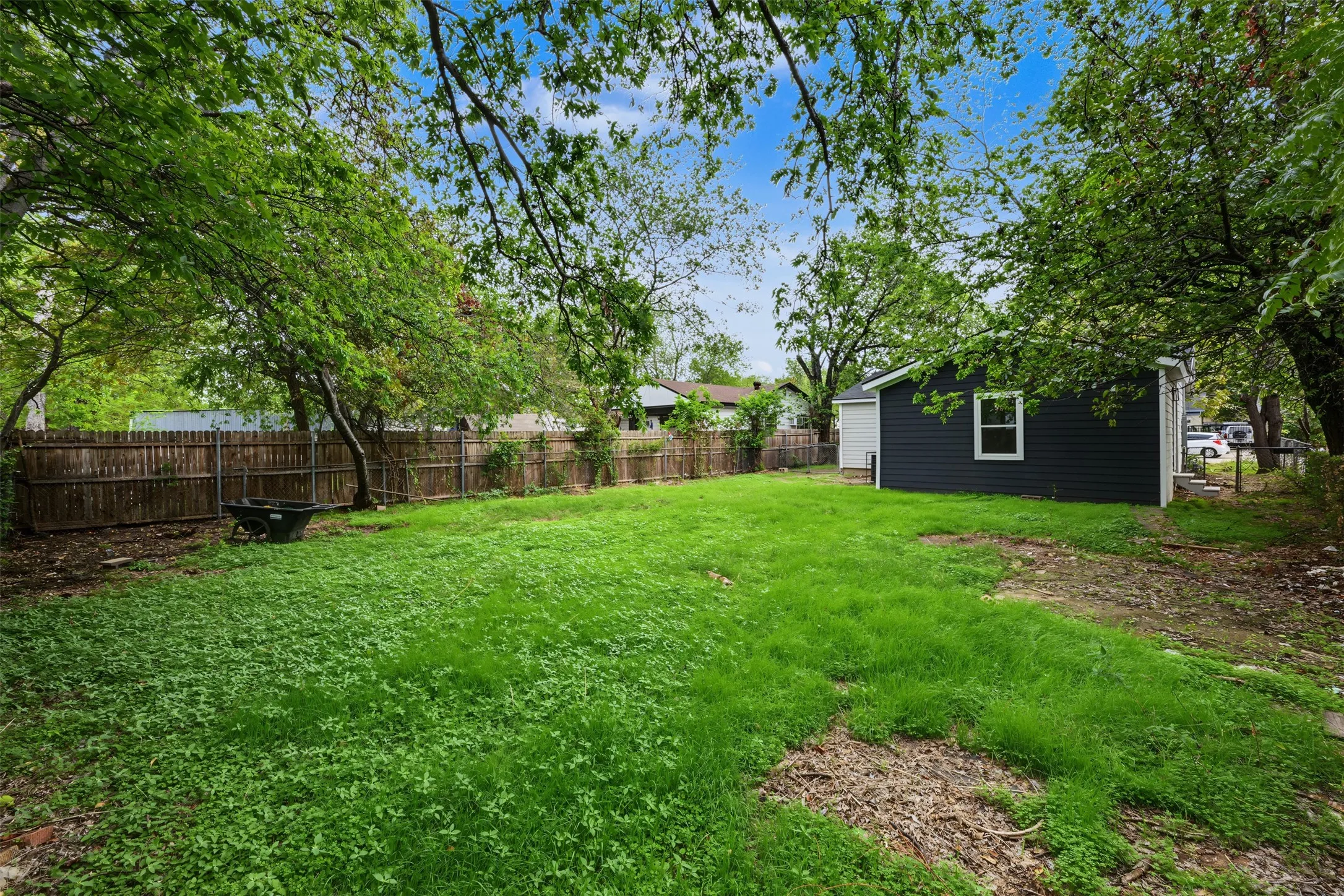Expansive backyard featuring a wood-panel fence, mature trees, and a detached structure with dark-tone siding