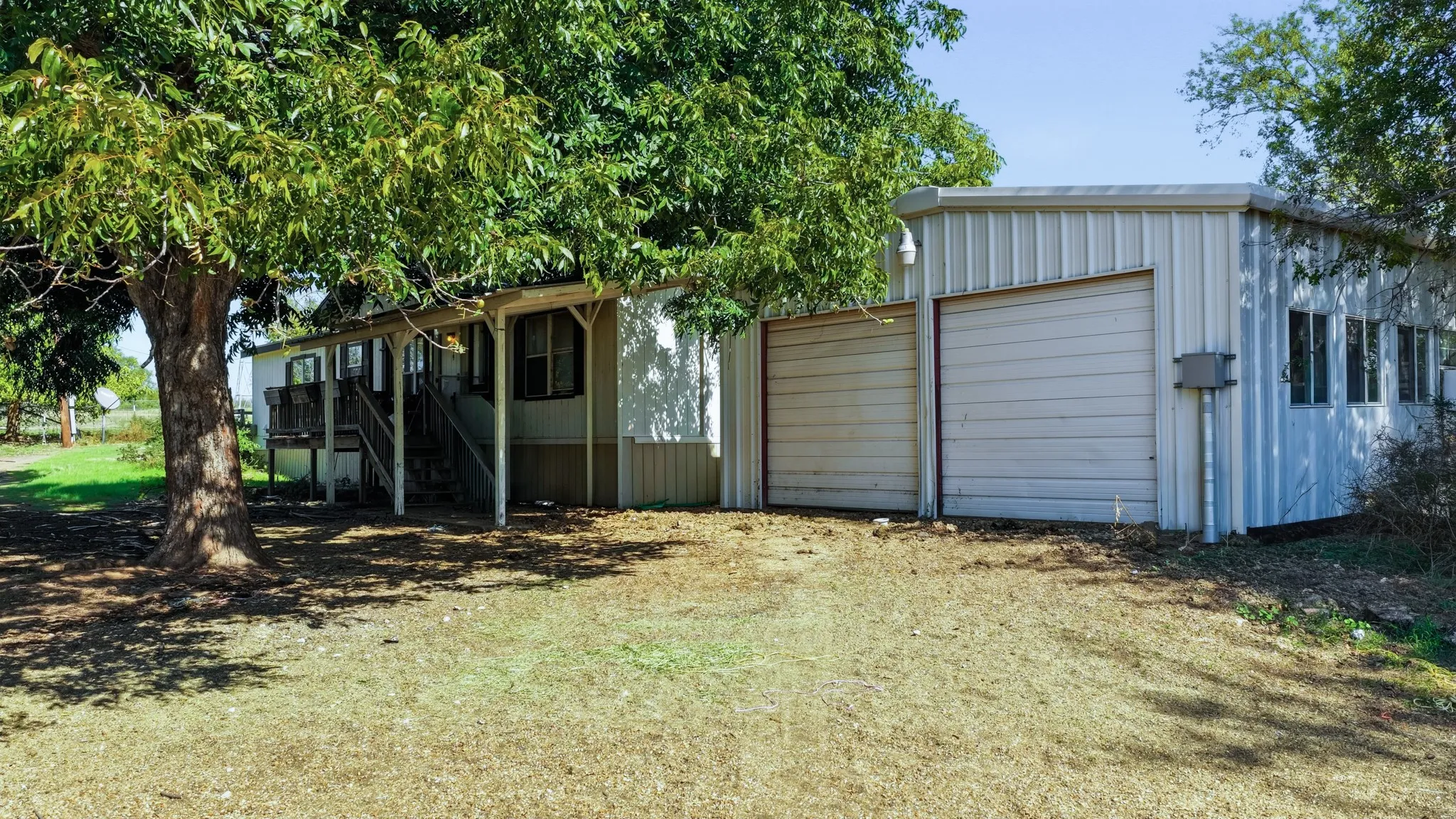 Exterior featuring a detached metal garage with dual roll-up doors, covered porch, and mature trees