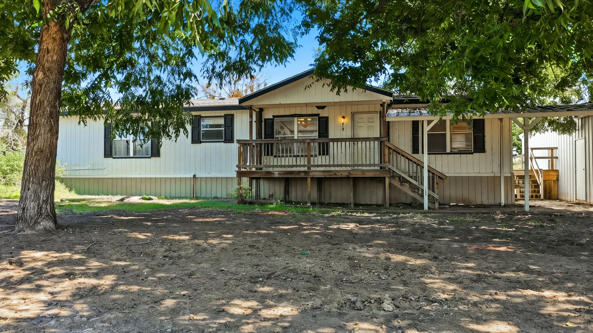 Single-story exterior featuring vertical siding, a raised wood deck with staircase, and an attached covered carport