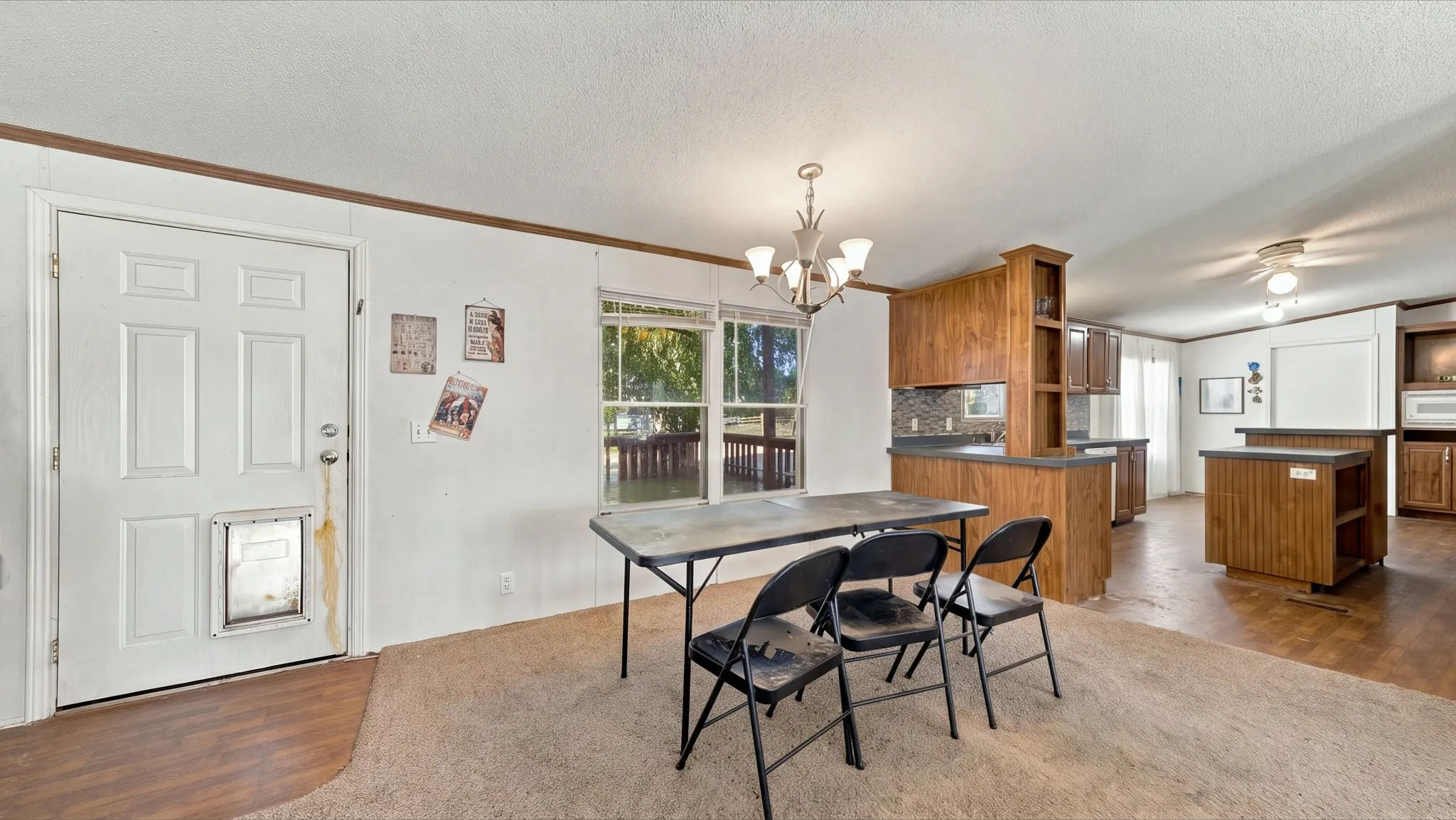 Open-concept interior featuring wood-finish cabinetry, built-in kitchen peninsula, multi-arm chandelier lighting, and dual-window natural lighting