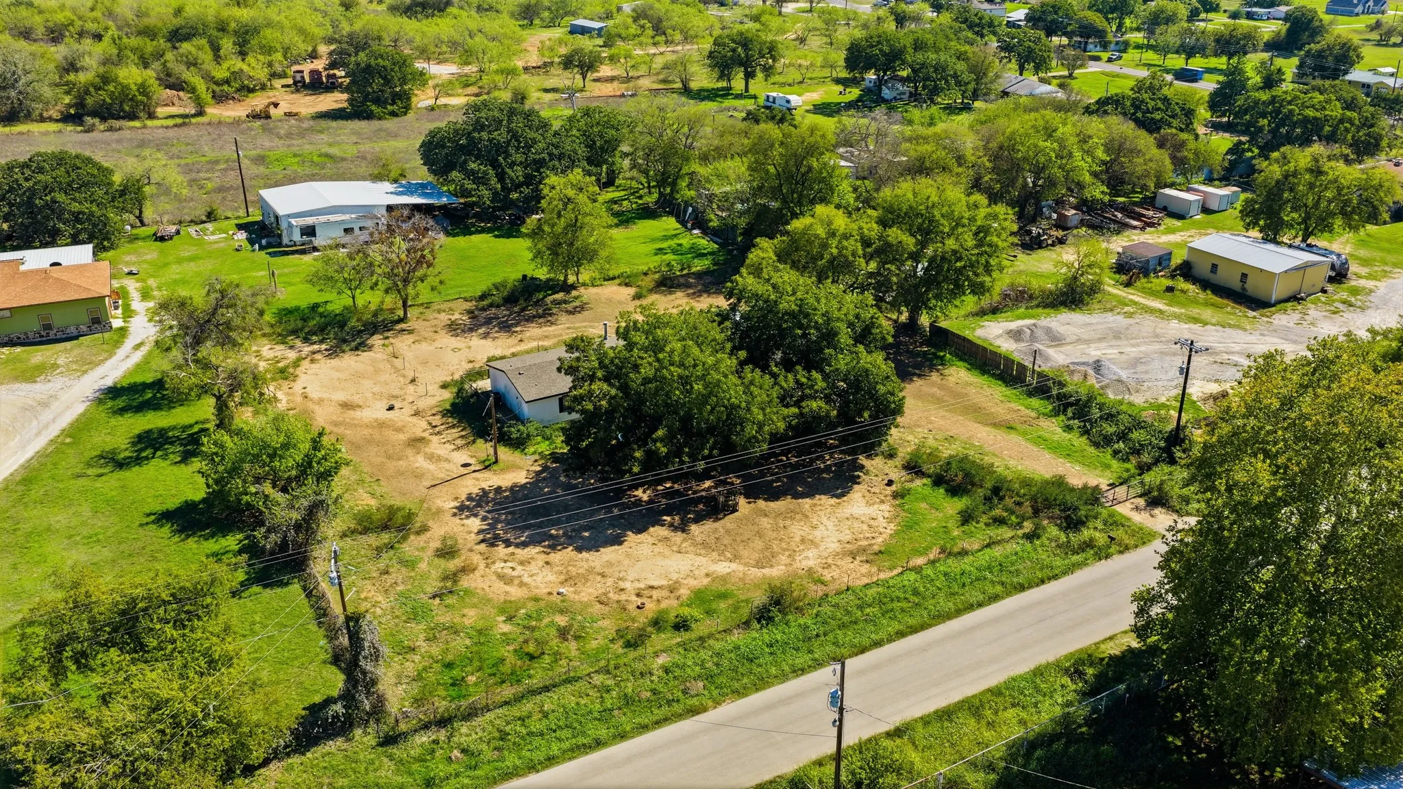 Aerial perspective of a sprawling lot featuring mature trees, open grassy areas, and paved road access