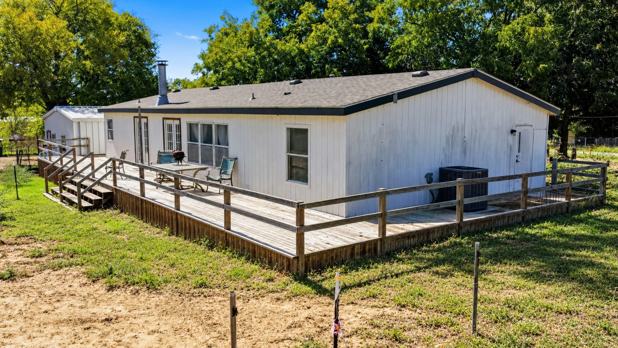 Wraparound wood deck with rail enclosure, exterior vertical panel siding, asphalt shingle roof, and detached storage structure