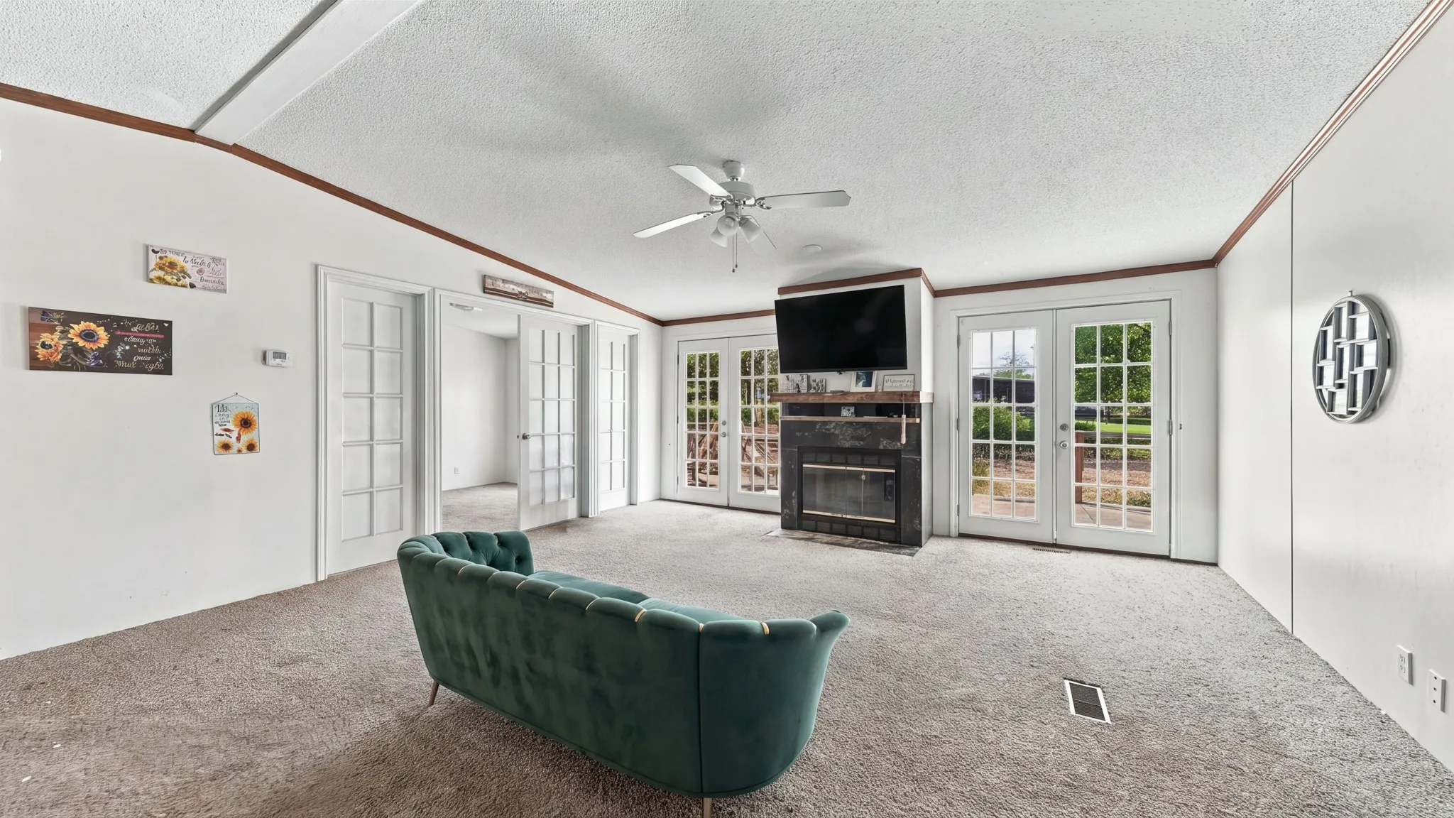 Fireplace with dark stone surround, multiple sets of French doors, ceiling fan, and carpeted flooring