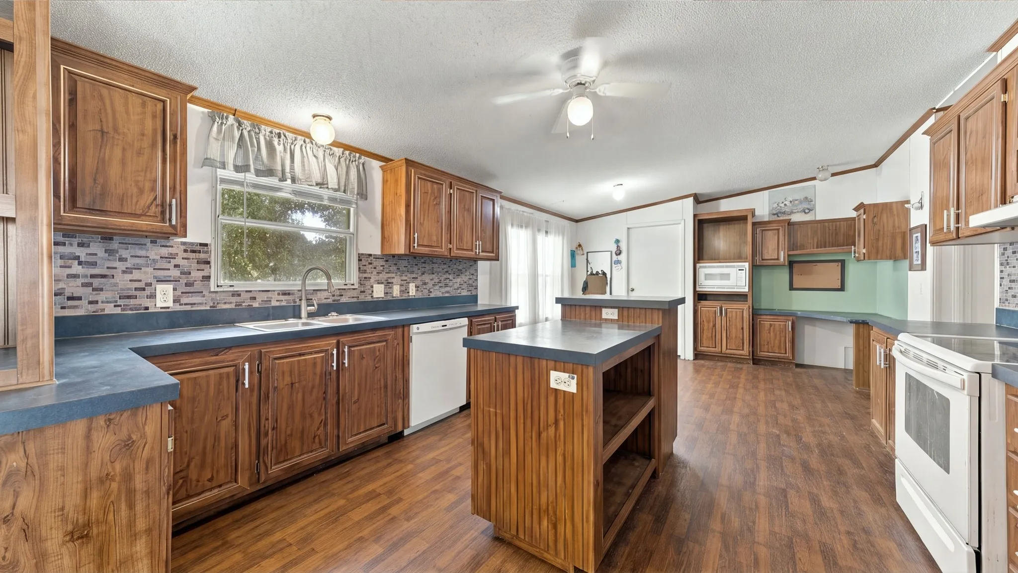 Kitchen featuring wood-finish cabinetry, a central island with storage shelving, tiled backsplash, and wood-finish flooring