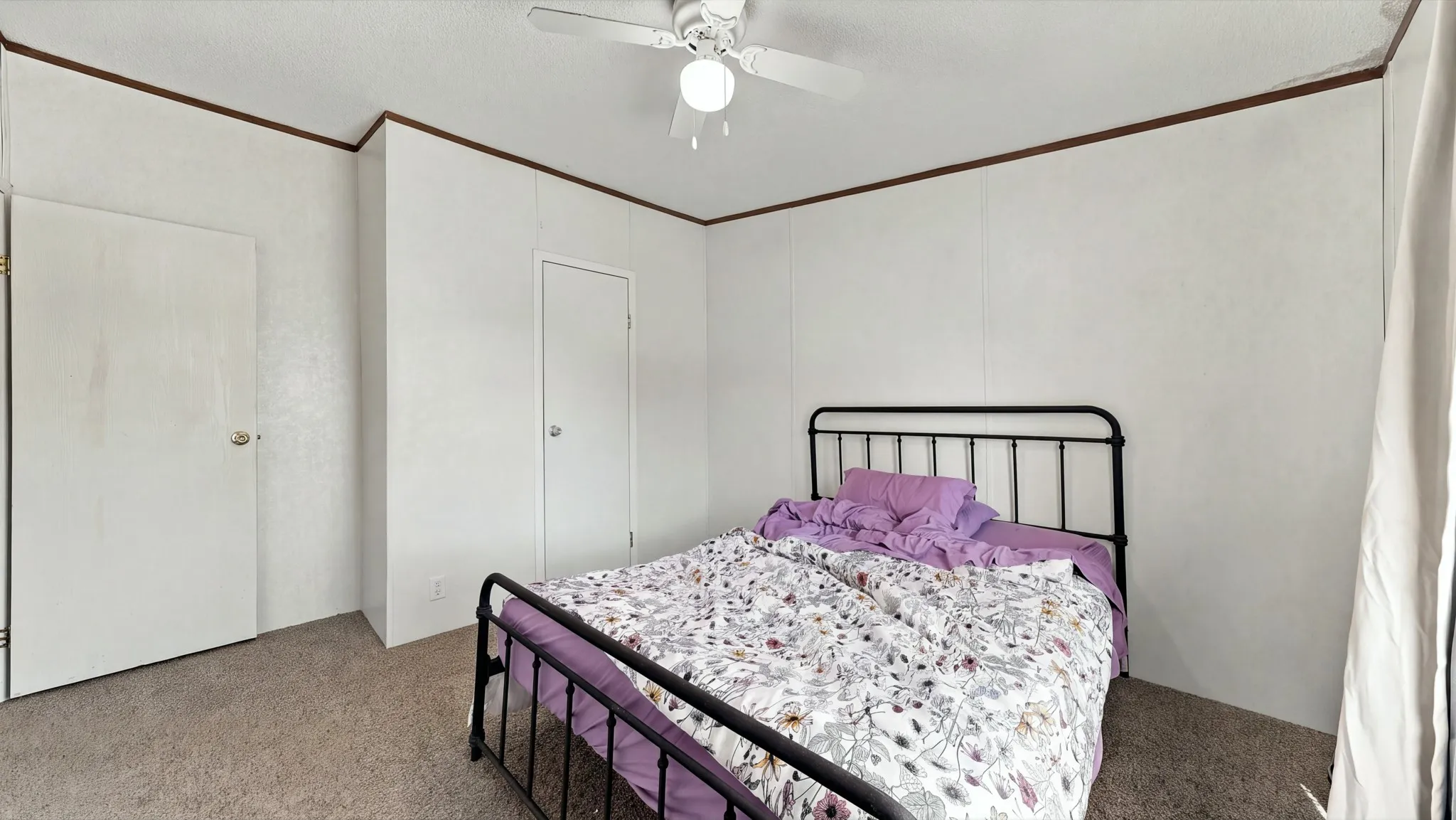 Room featuring neutral wall paneling, carpeting, two doors with metallic hardware, and a ceiling-mounted light fixture with a fan