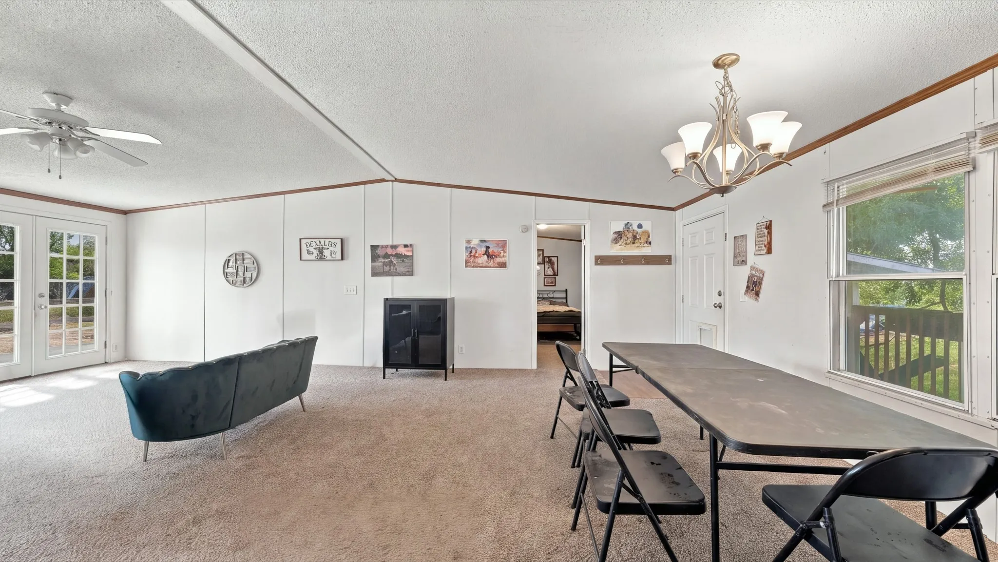 Spacious interior featuring vaulted ceilings, a central multi-arm chandelier, ceiling fan, carpeted flooring, and glass-paneled double doors