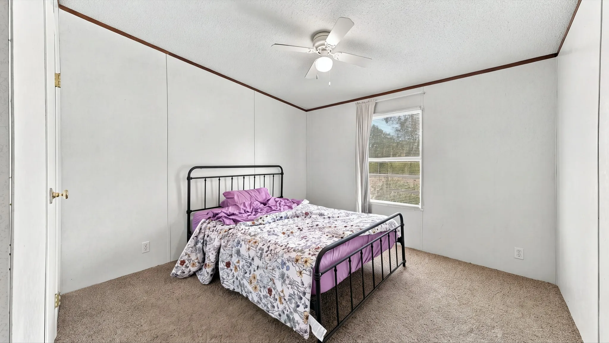 Neutral wall-paneling, wall-to-wall carpeting, ceiling fan with integrated lighting, and a single-pane window