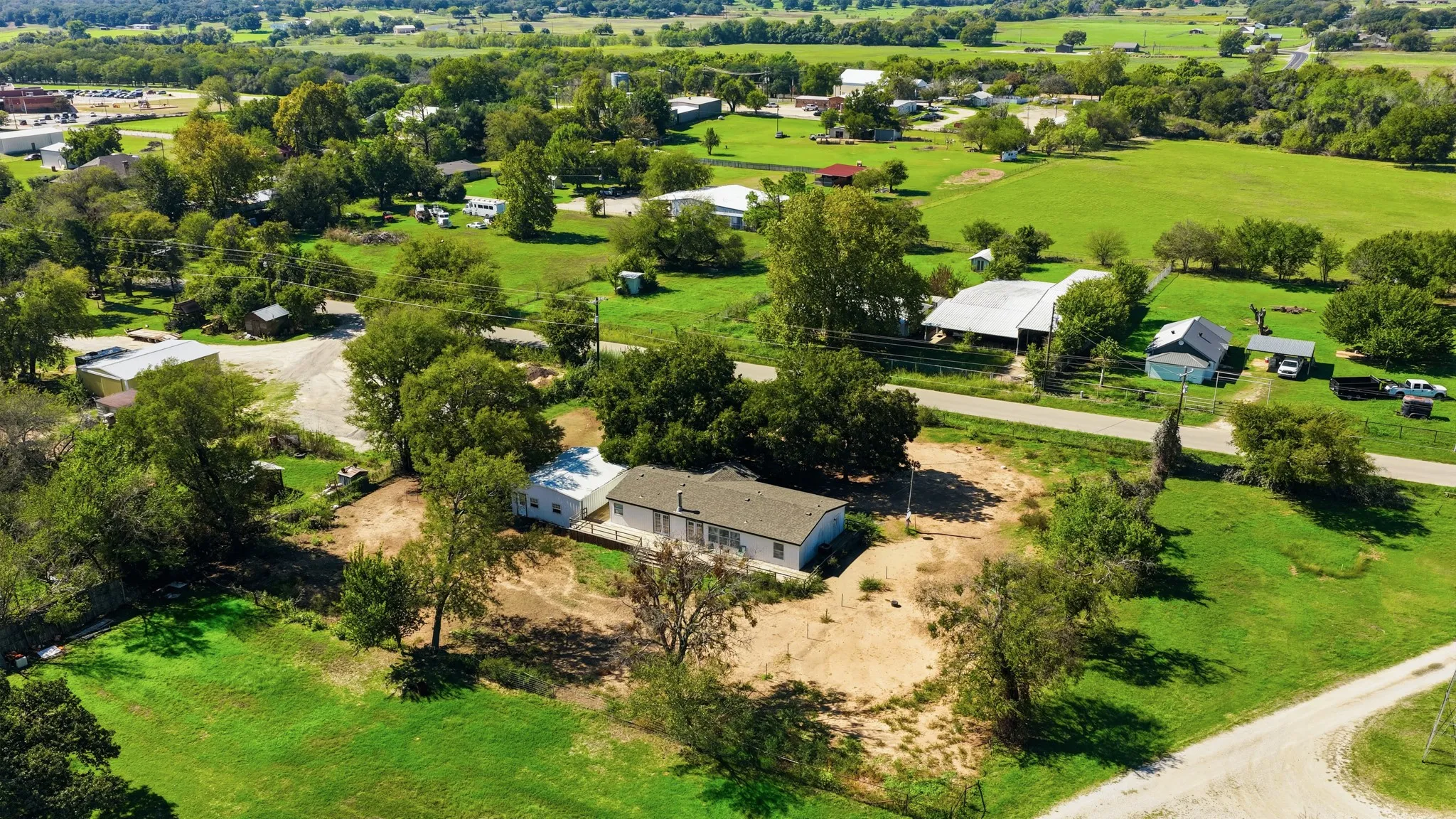 Aerial perspective of a detached residence featuring a neutral-toned exterior, a pitched roof, and expansive acreage comprised of mature trees and open pasture