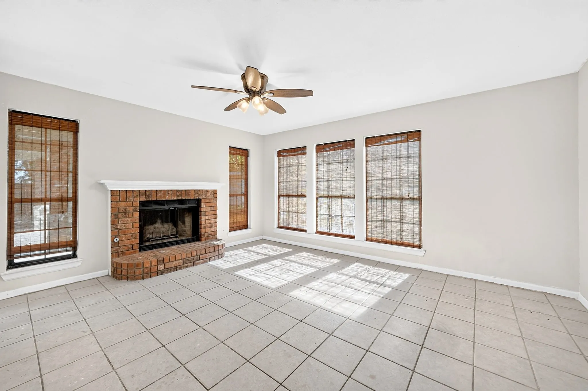 Brick fireplace with a raised hearth, large-format tile flooring, and a ceiling fan with integrated lighting