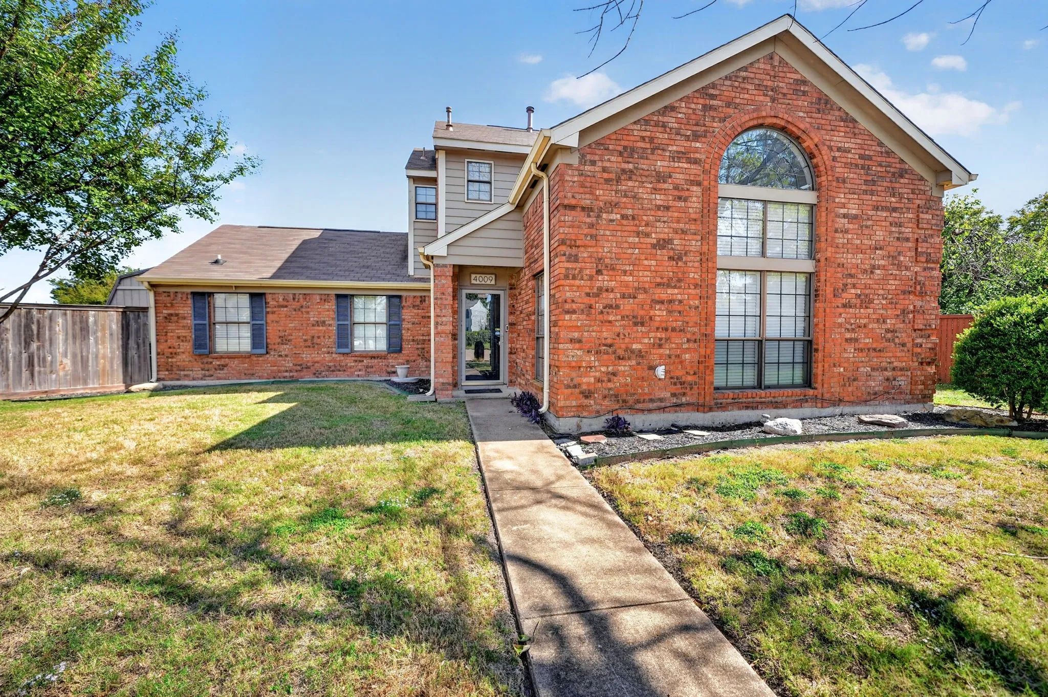 Two-story brick exterior featuring a prominent arched window, horizontal siding accents, dark-toned shutters, and a concrete walkway