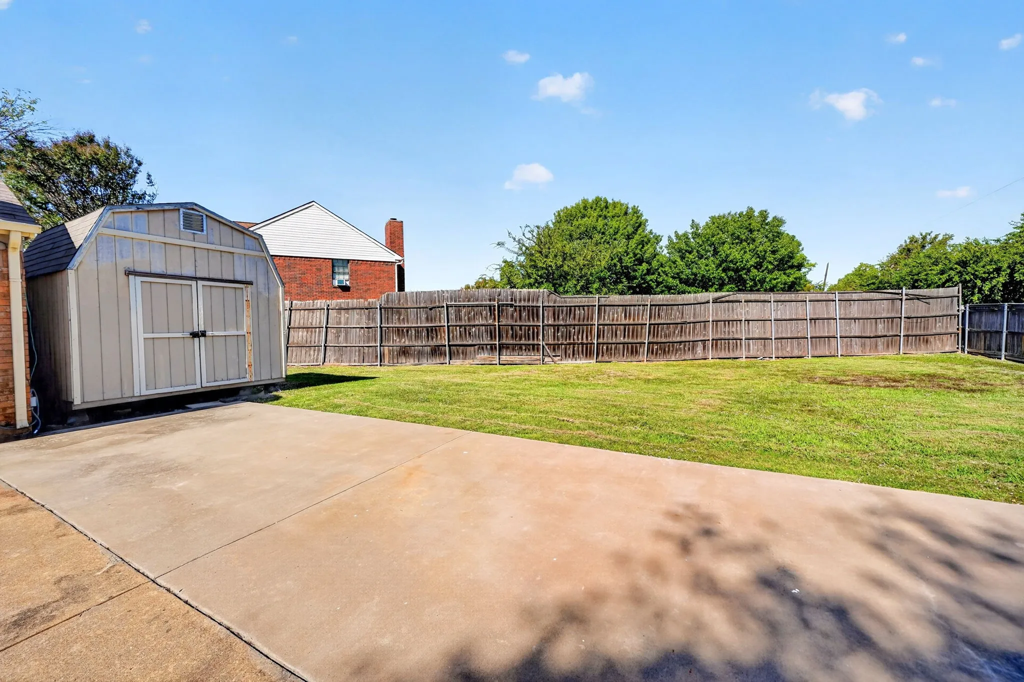 Backyard storage building and featuring a concrete patio, grassy lawn, wood privacy fencing, and an exterior storage shed