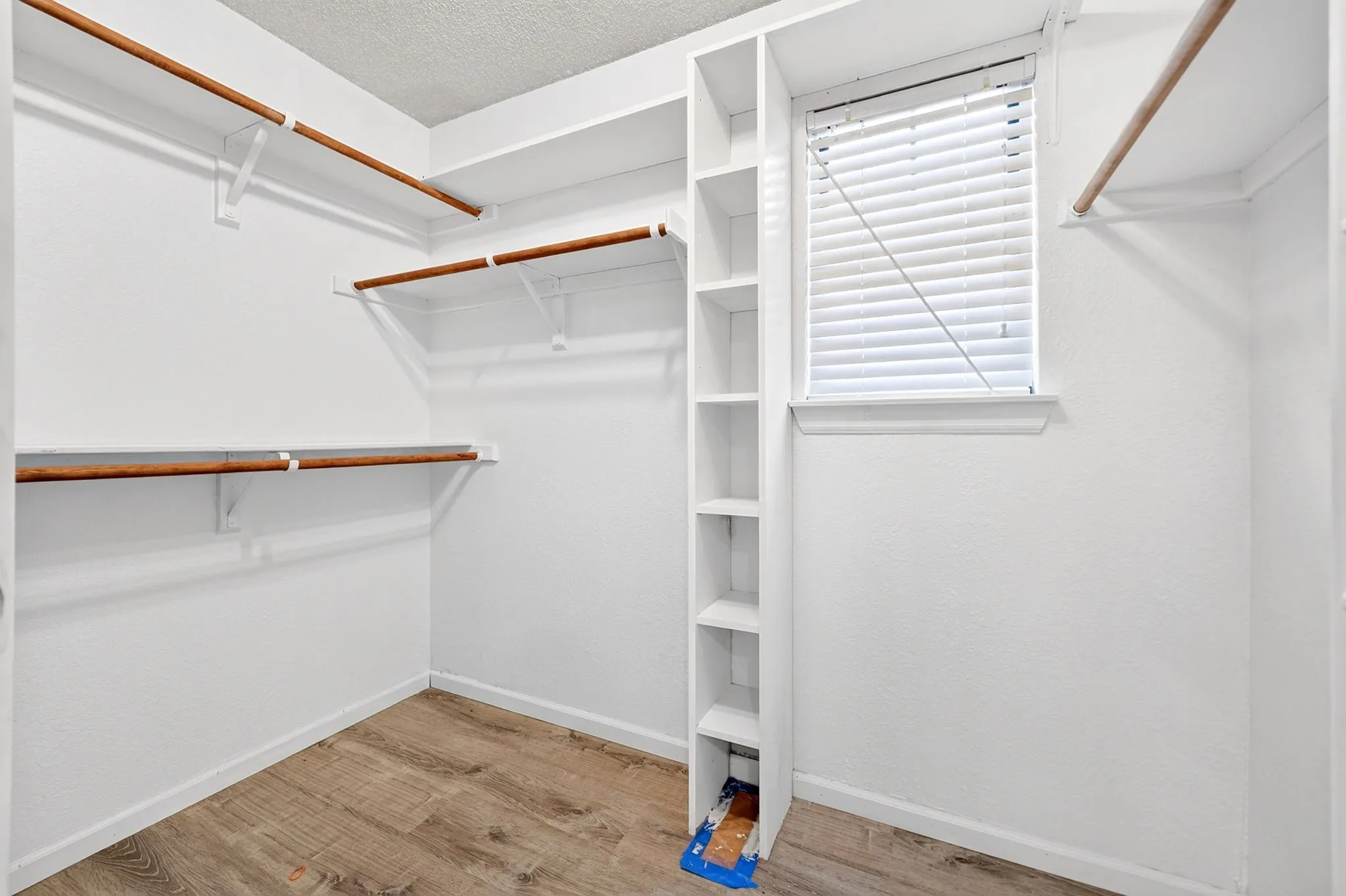 Walk-in closet featuring wood-finish flooring, multi-level shelving, integrated vertical storage cubbies, and a window with horizontal blinds