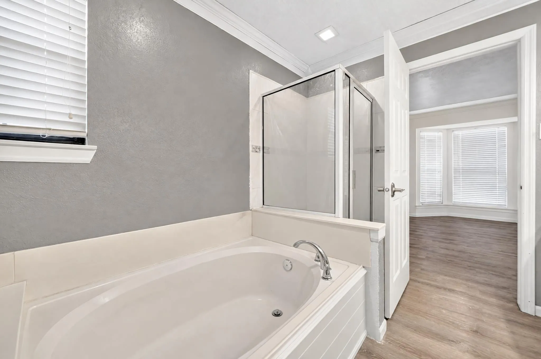 Soaking tub with chrome faucet, glass-enclosed shower, crown molding, and wood-finish flooring