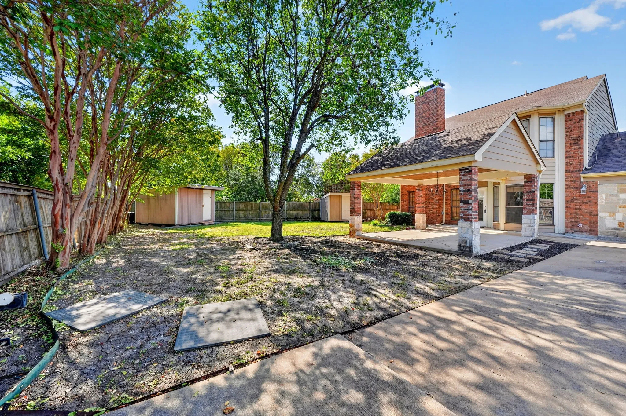 Backyard featuring a covered patio, brick masonry exterior, stone-accented support columns, and detached storage structures