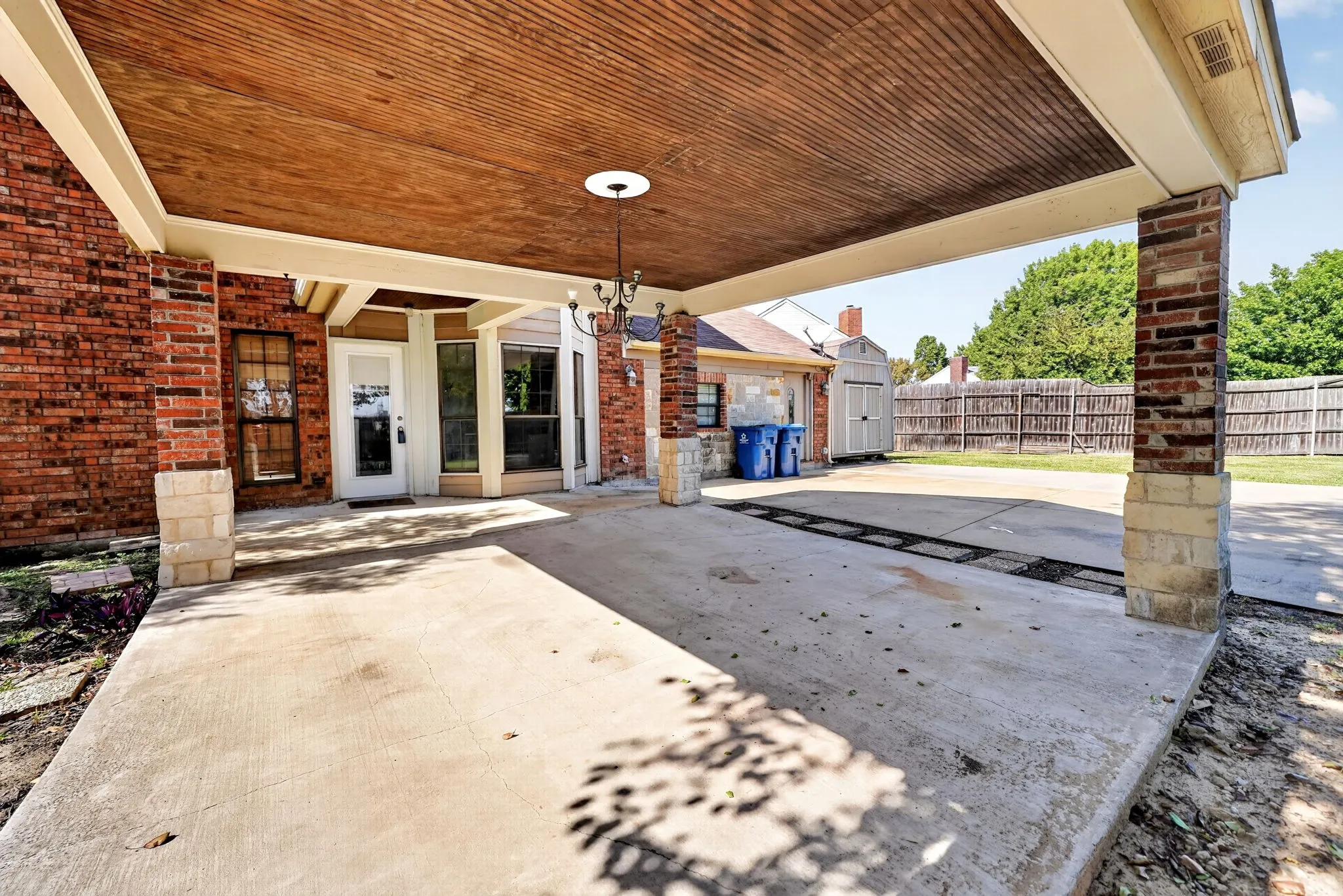 Covered patio featuring a wood-plank ceiling, brick and stone masonry pillars, and an attached chandelier