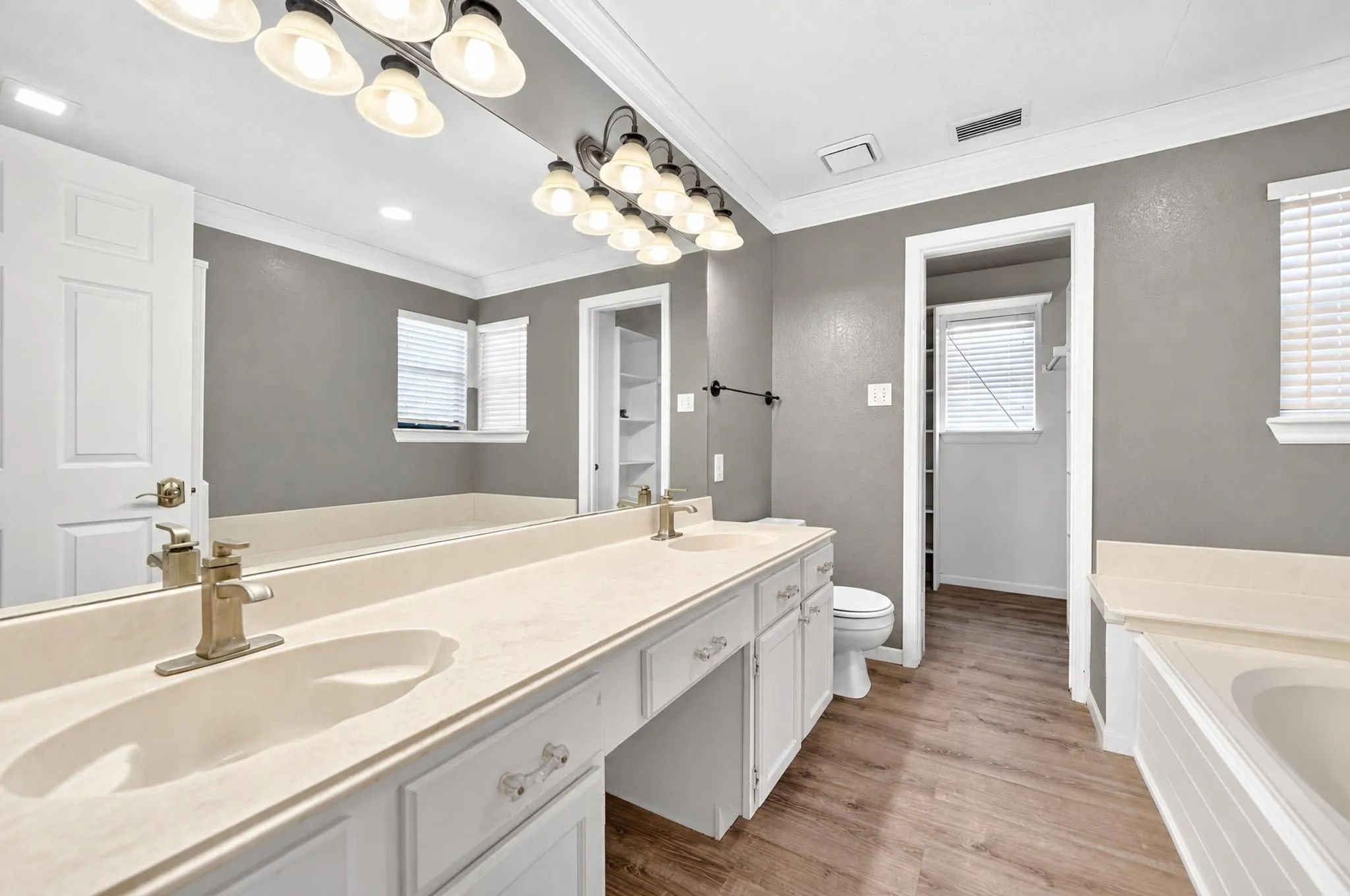 Dual-sink vanity with solid surface countertop, wood-finish flooring, full-width wall mirror, and integrated soaking tub