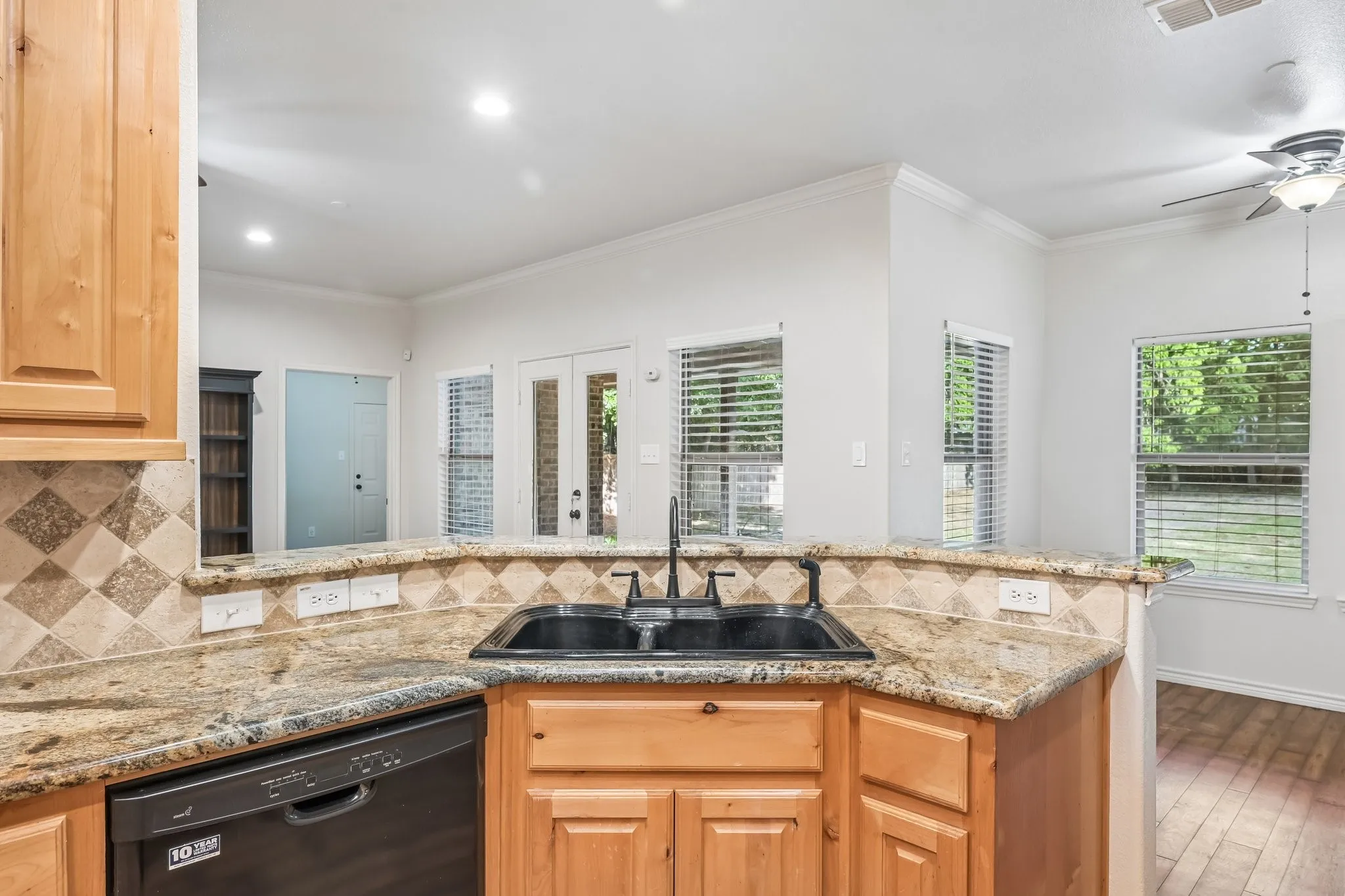 Kitchen featuring wood cabinetry, a double basin sink with a black faucet, and granite countertops with a tile backsplash
