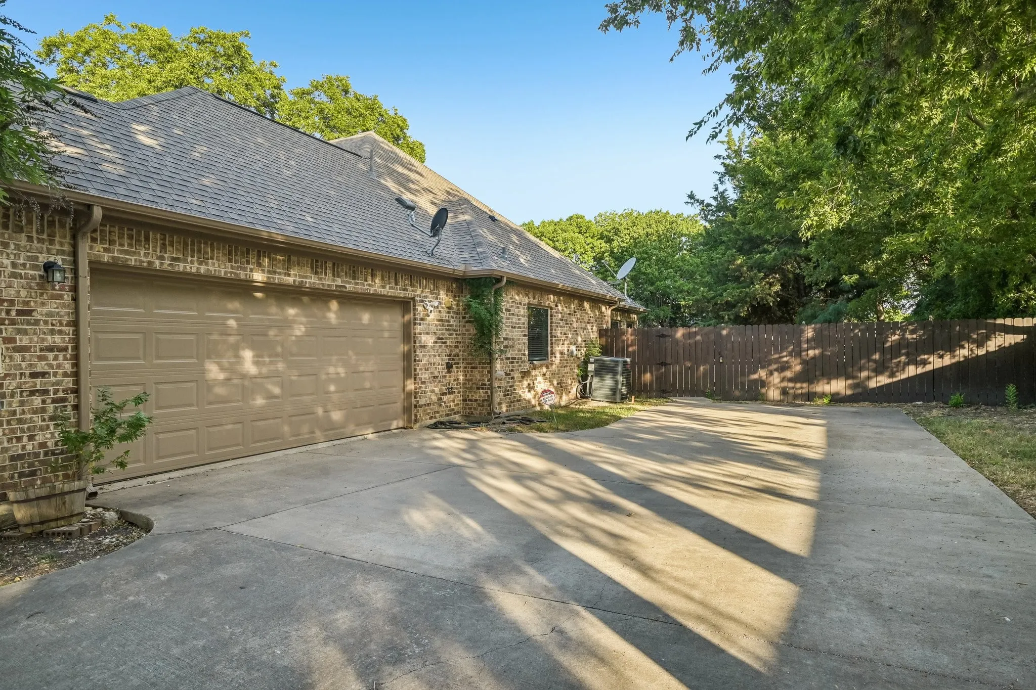 Brick exterior with a multi-car concrete driveway, attached garage, and a privacy fence